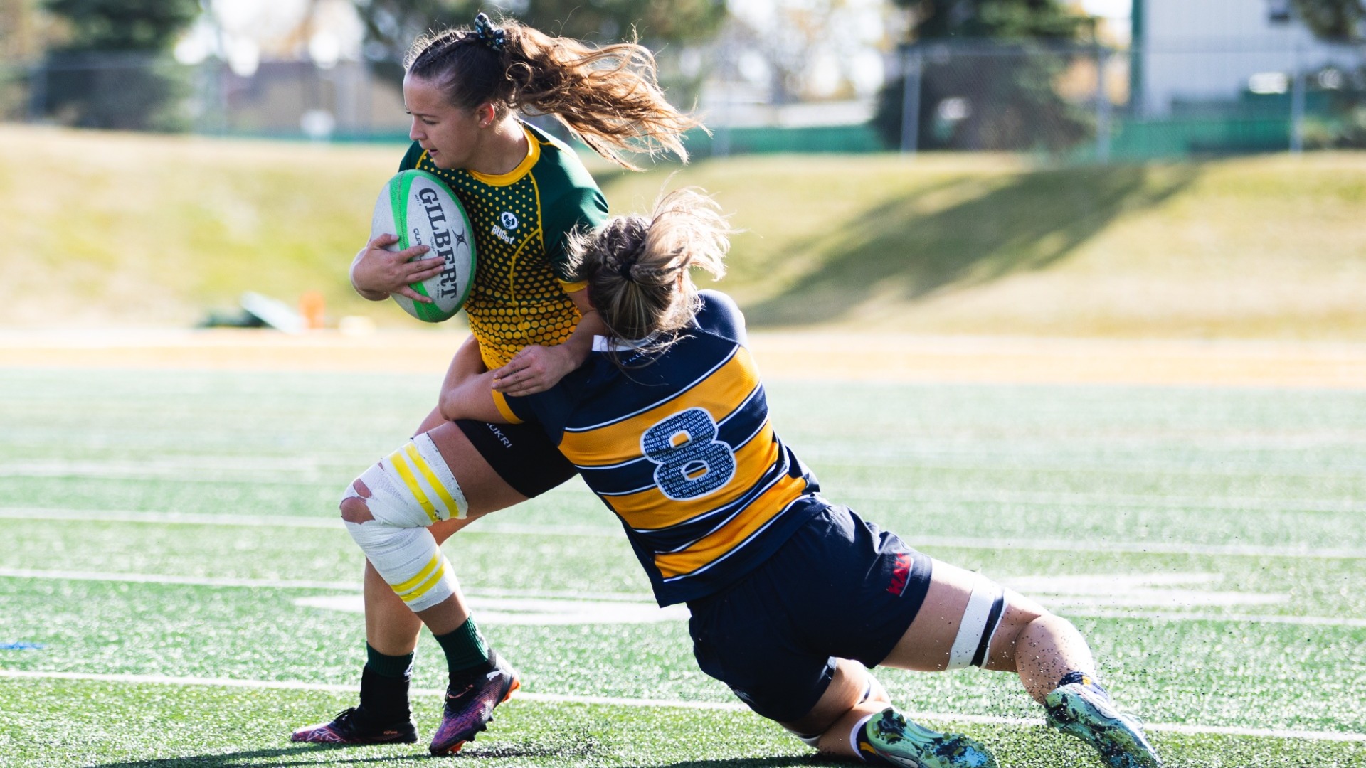 An Alberta player running with the ball tries to avoid being dragged down by a UBC defender