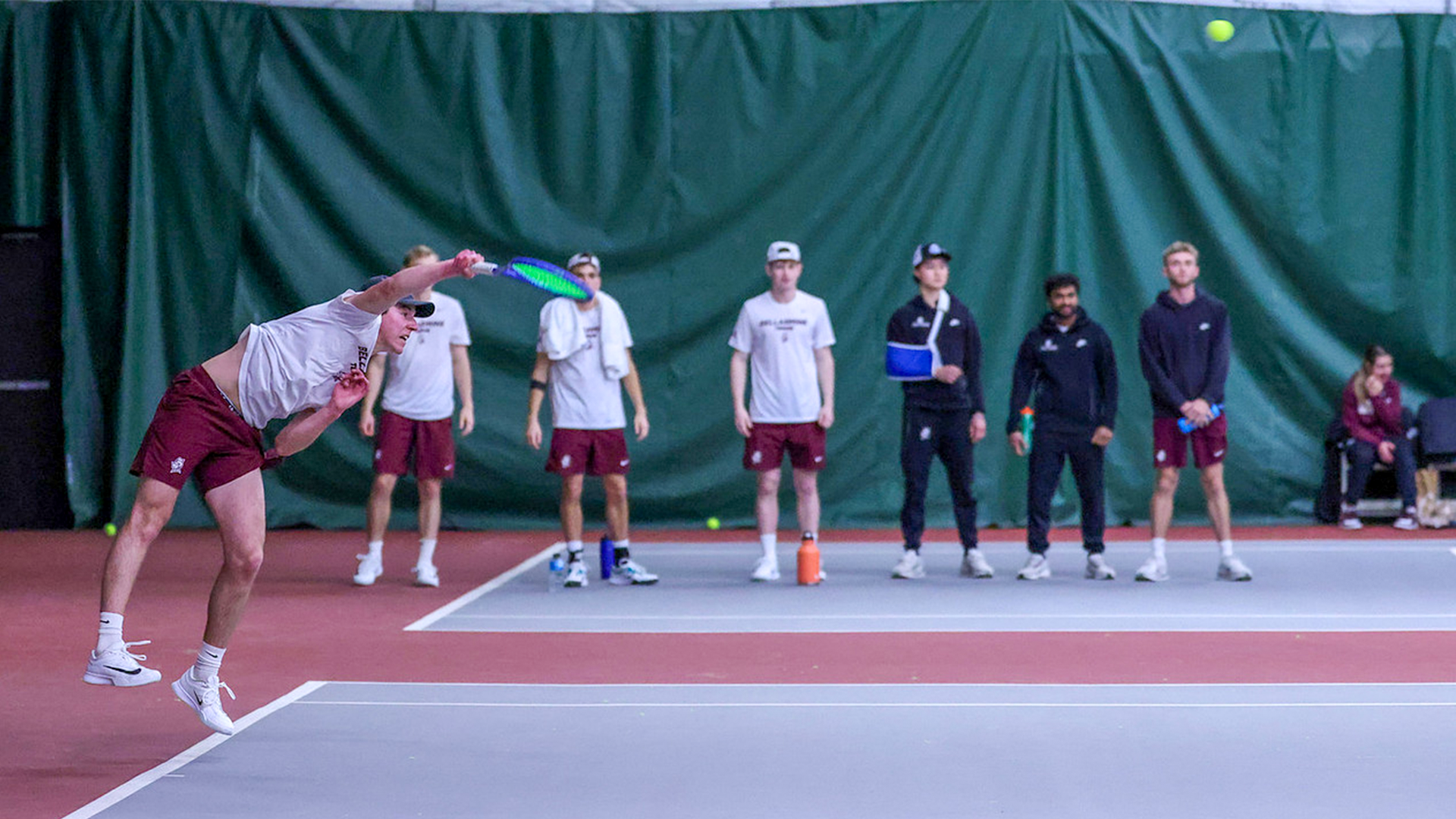 Colby Berson serves to his EKU opponent with his teammates watching in the background