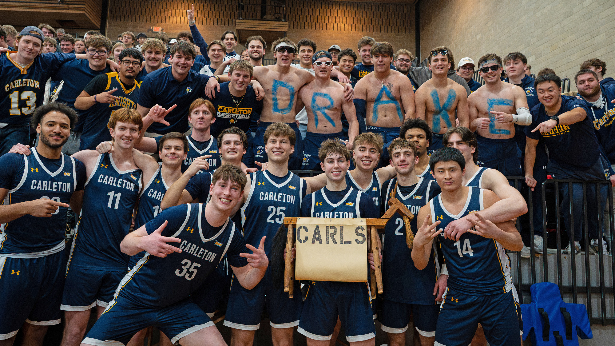 Carleton men's basketball team holds the Goat Trophy in front of celebrating fans