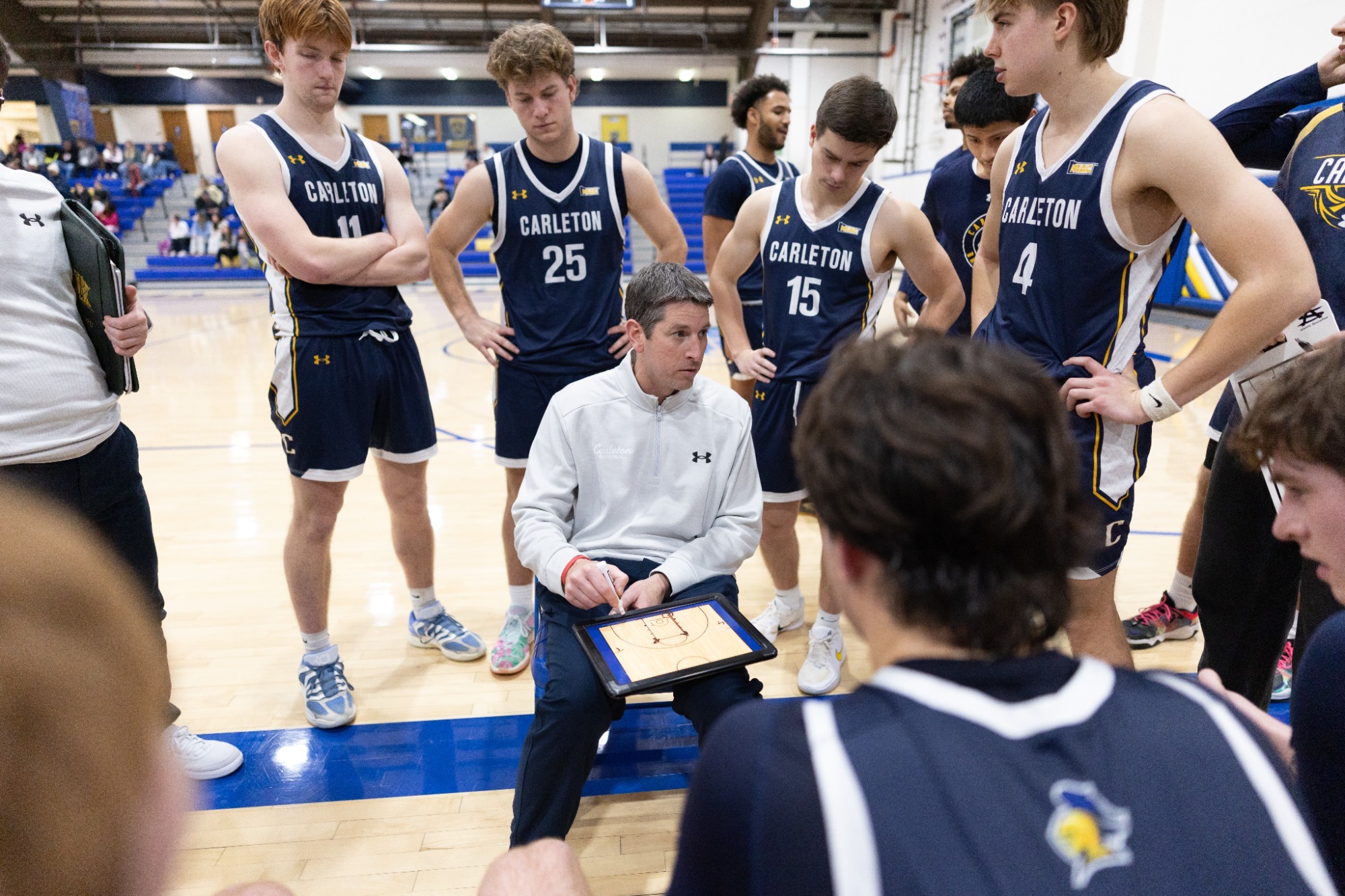 MBB Head Coach Ryan Kershaw draws up a play for his team in a huddle