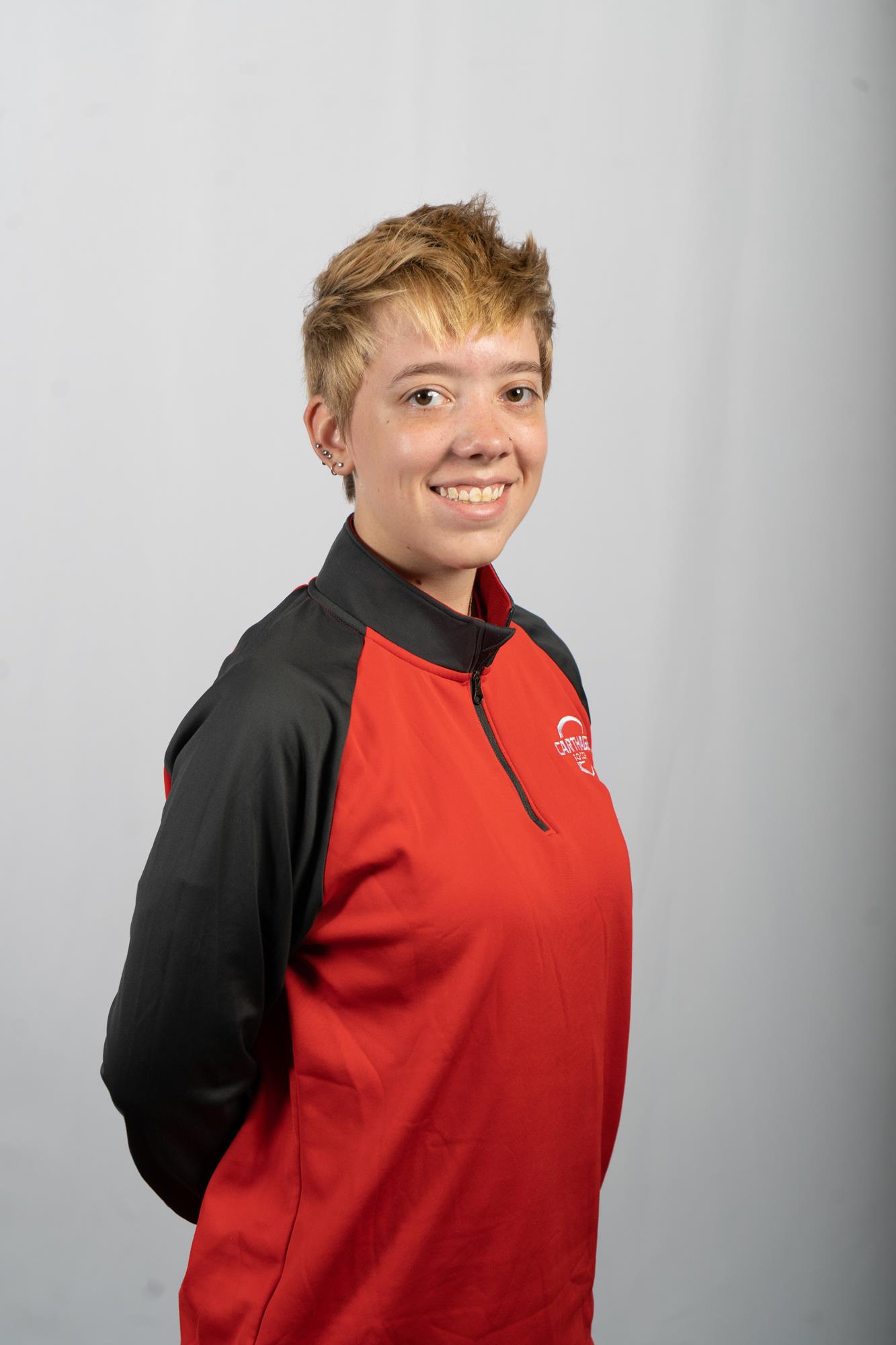 Maddie Punzel smiling for their women's soccer headshot, wearing a grey and red warmup jacket.