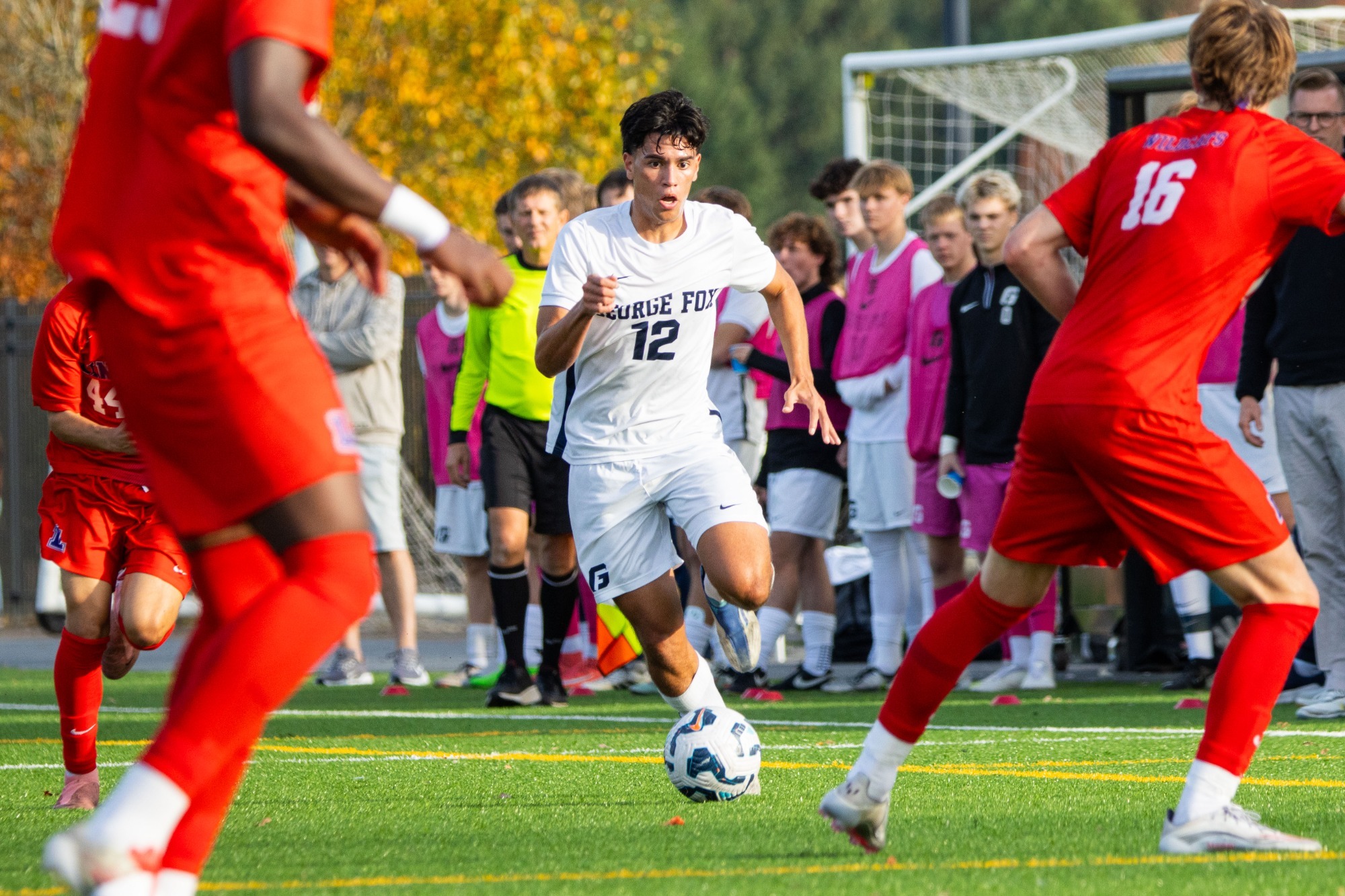 Elijah Soon dribbling ball between defenders with GFU bench in background