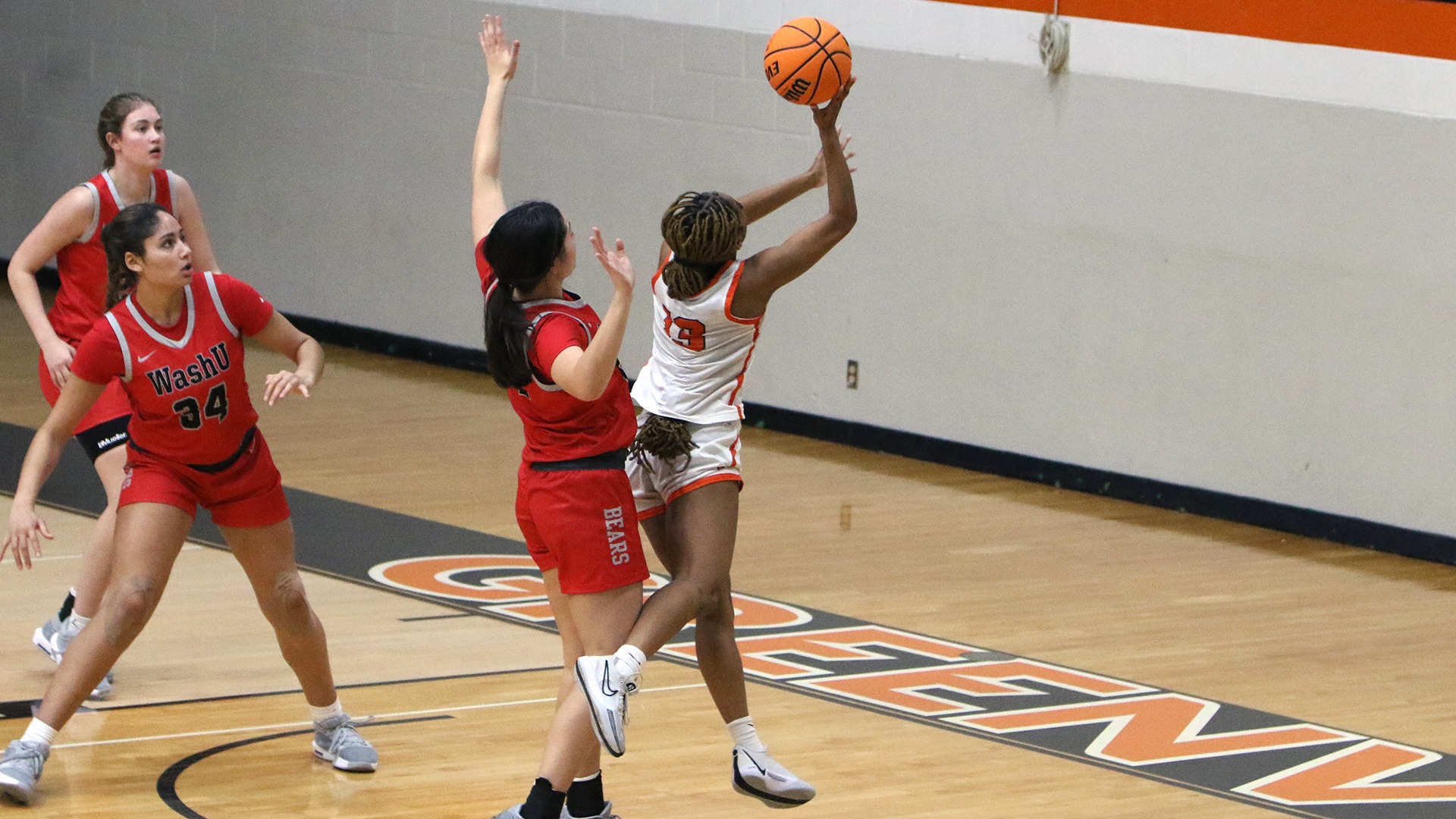 Mya Mann in white jersey going up for a layout with a WashU player in red trying to defend her. 