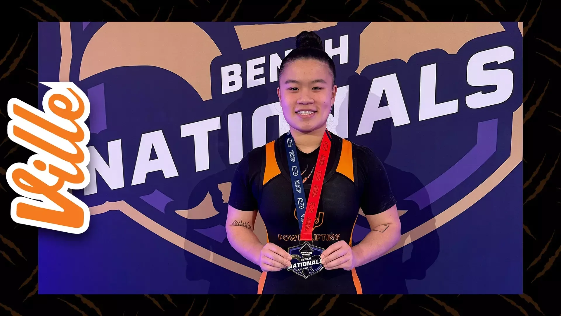 Young Asian woman with brown hair and brown eyes. She is holding a black medal and wearing an orange and black singlet.
