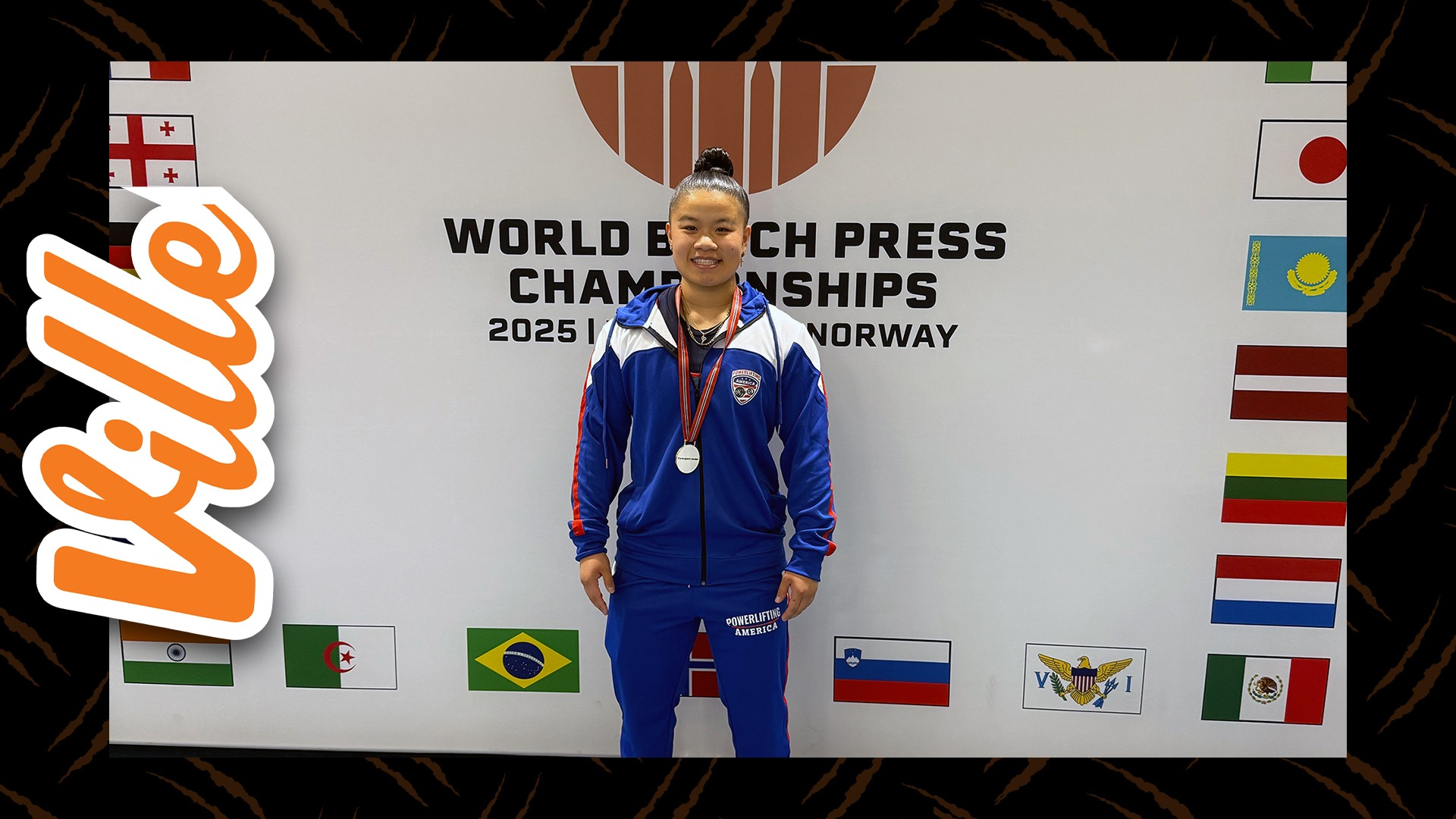 A young asian woman with brown hair and brown eyes stands with a medal around her neck. She wears a blue tracksuit. 