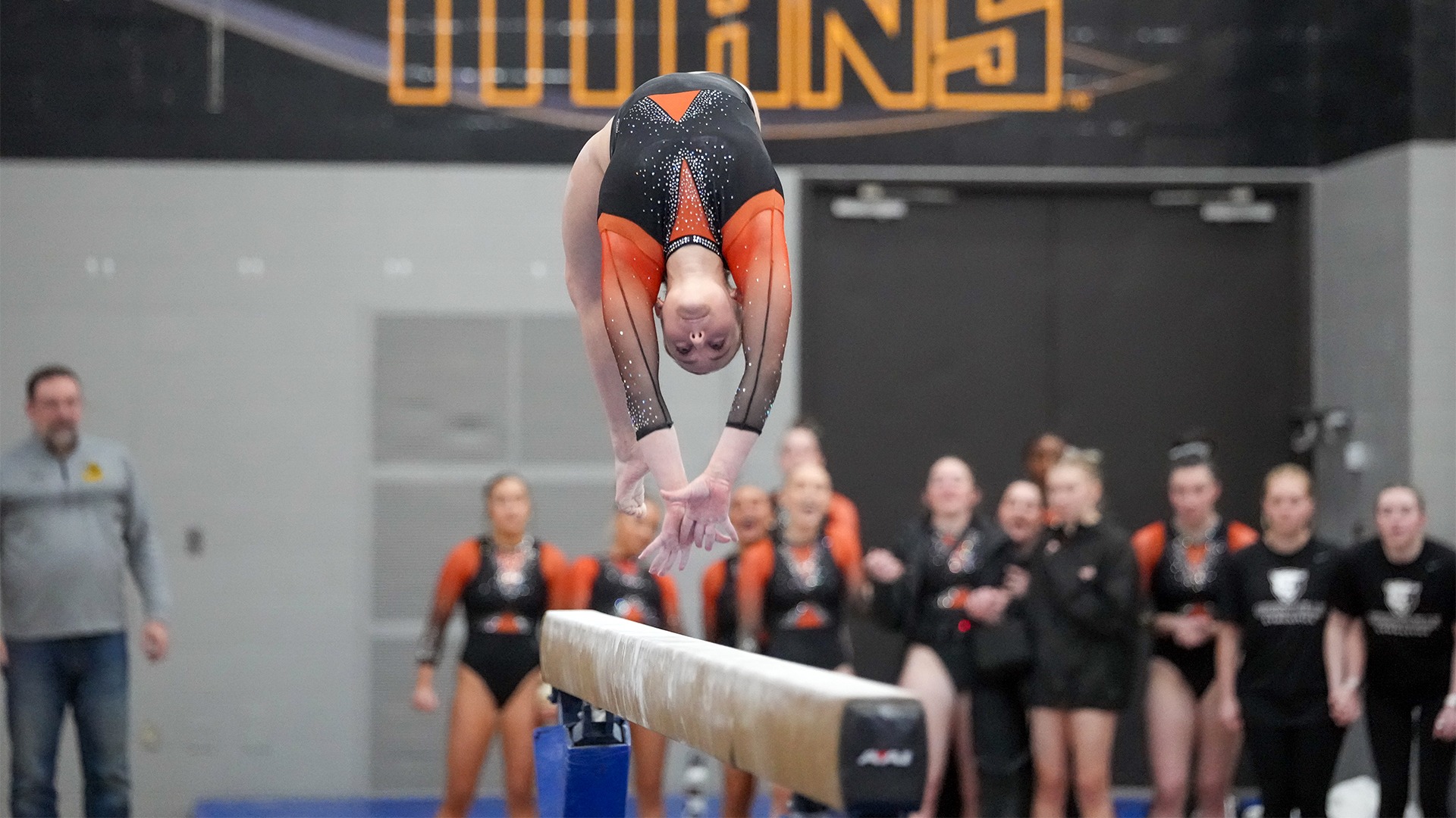 women's gymnast in black and orange leotard in air on beam