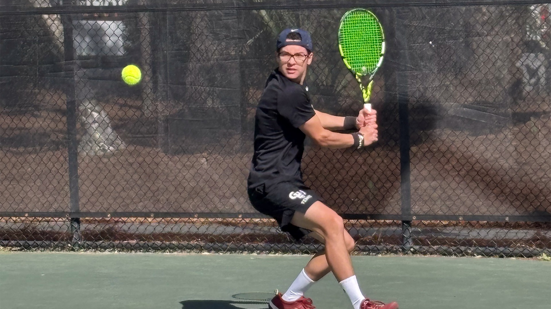 Jean Sanabria in black shirt and orange shirts hitting ball with racquet