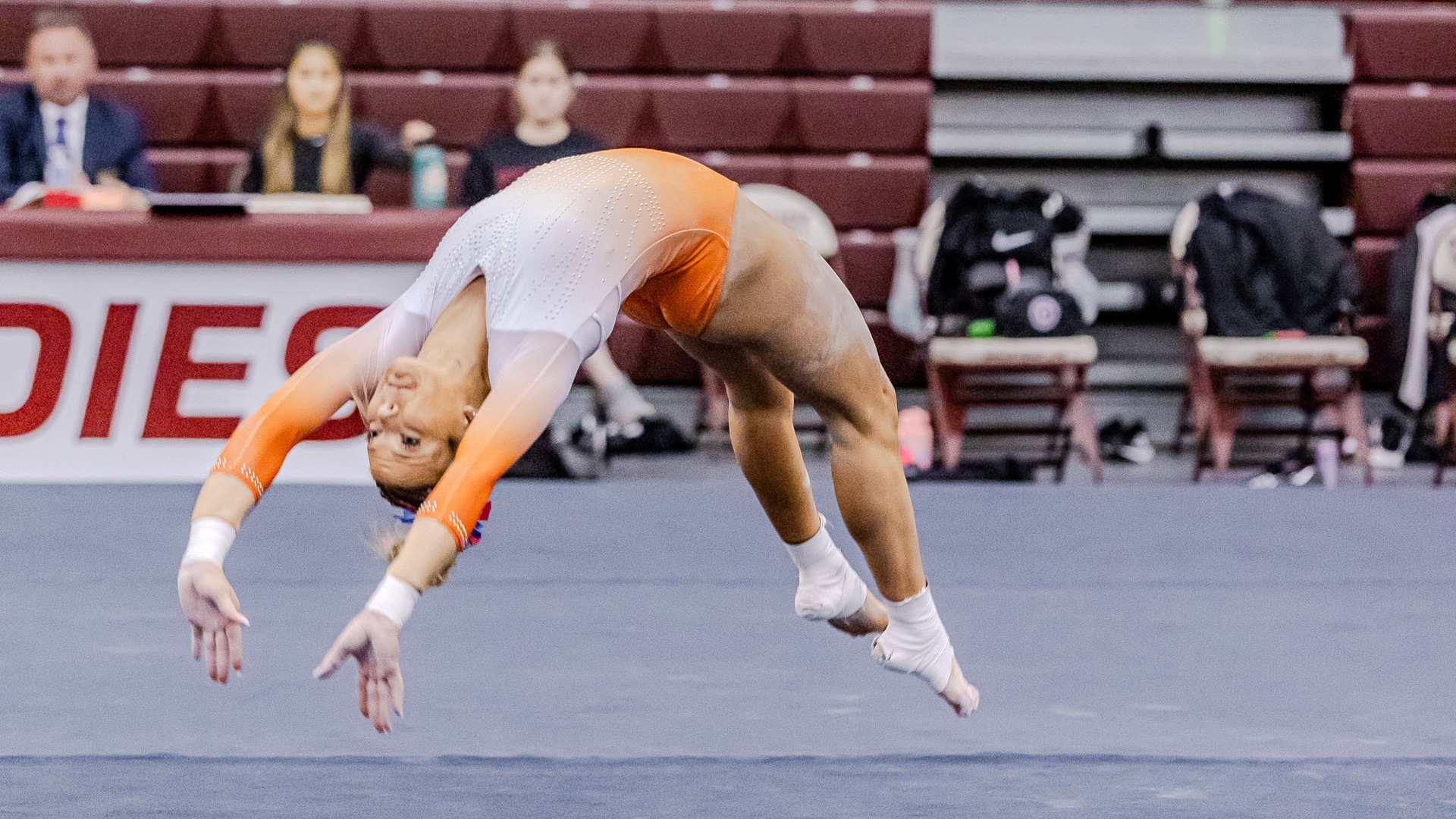Panther gymnast in white and orange leo doing backhand spring on floor