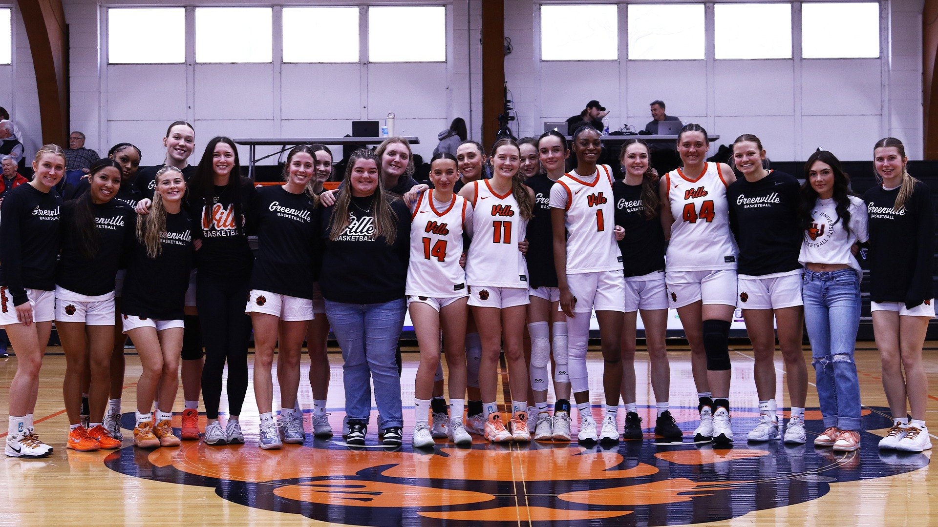 Group picture of women's basketball team with seniors in white jerseys and everyone else in black warmups