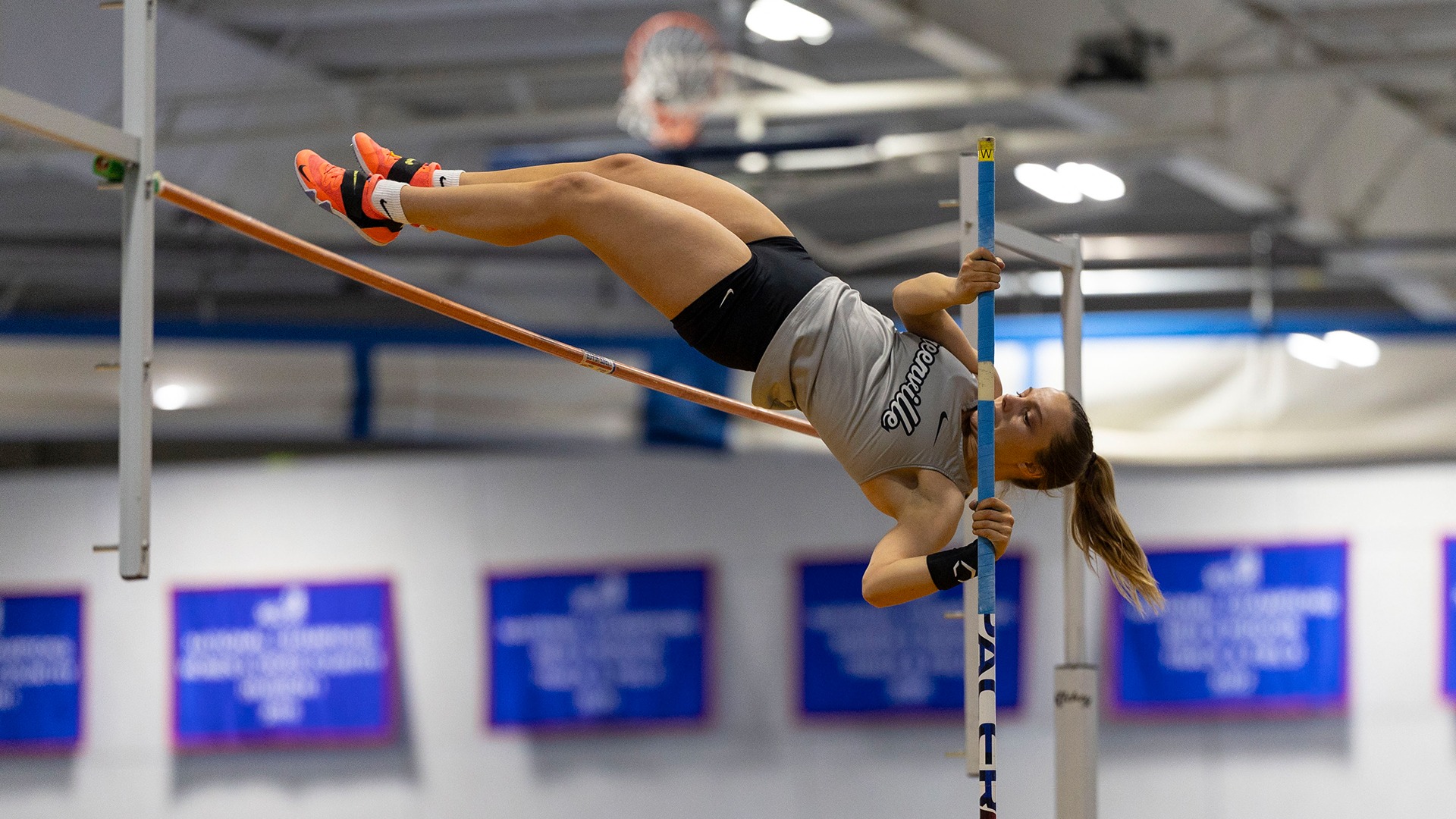 Farrow in grey uniform pole vaulting over bar