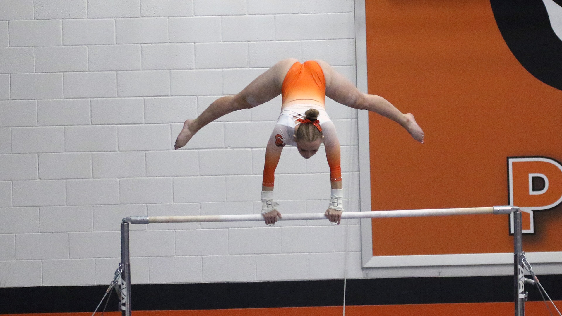 Panther woman gymnasts in orange and white leo upside down on bars