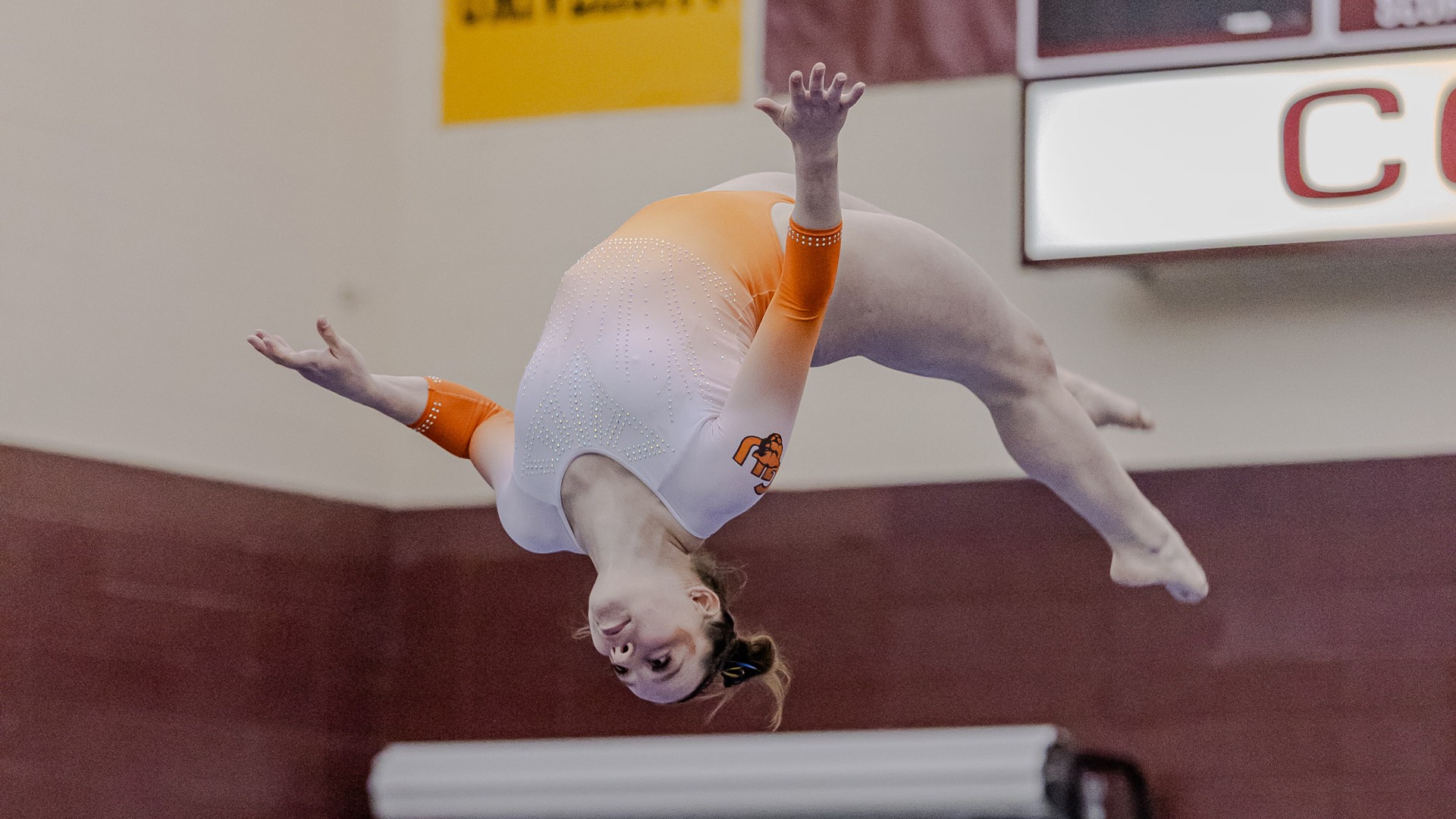 Amara Nelson in white and orange leo flipping on beam 