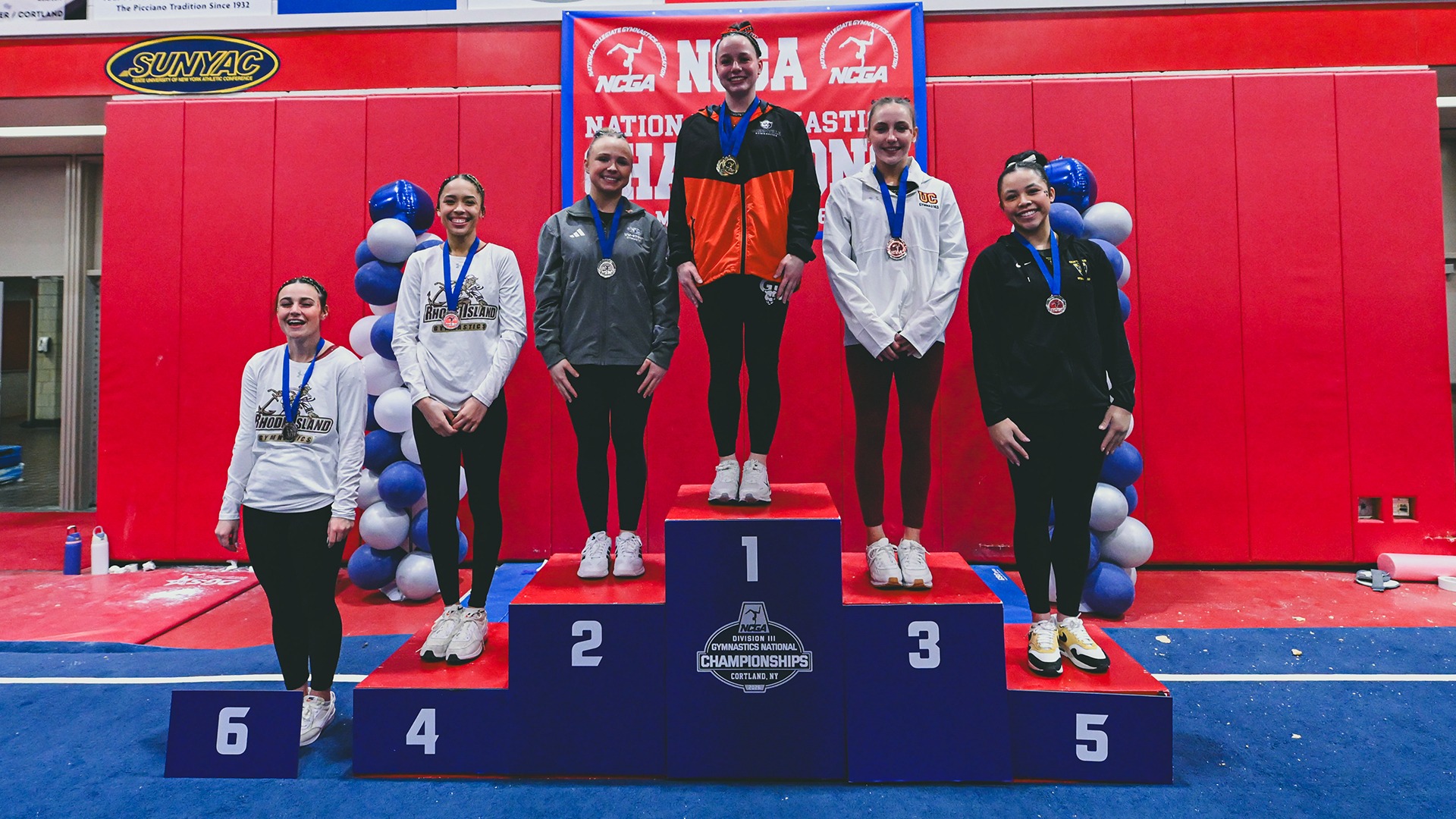 Amara Nelson in orange and black outfit with medal around neck on top podium spot
