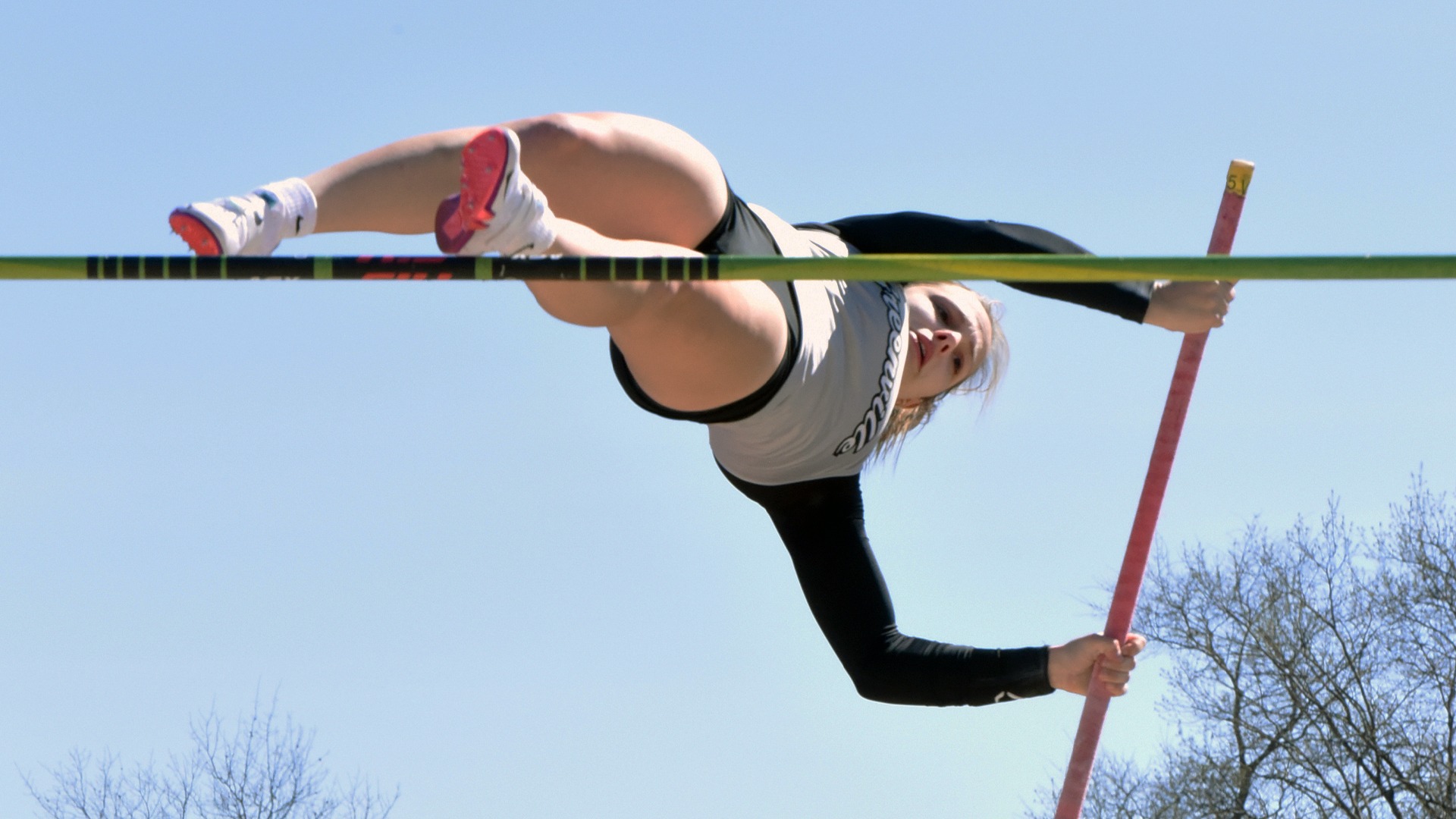 Woman panther in grey uniform pole vaulting
