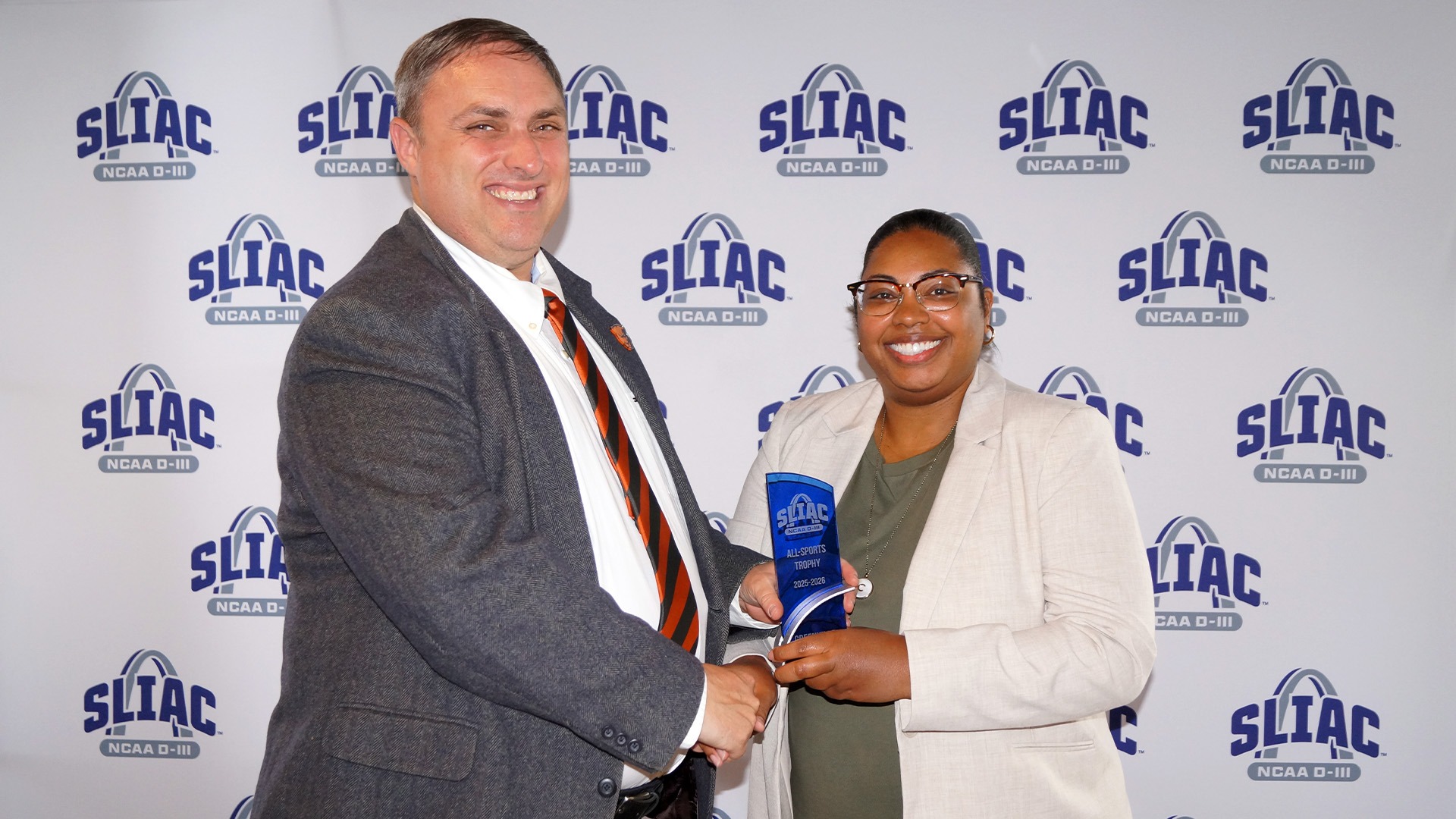 AD, B.J. Schneck, in suit and tie holding SLIAC All-Sports Trophy, while shaking SLIAC Commissioner, Chassidy Holloway's, hand. 