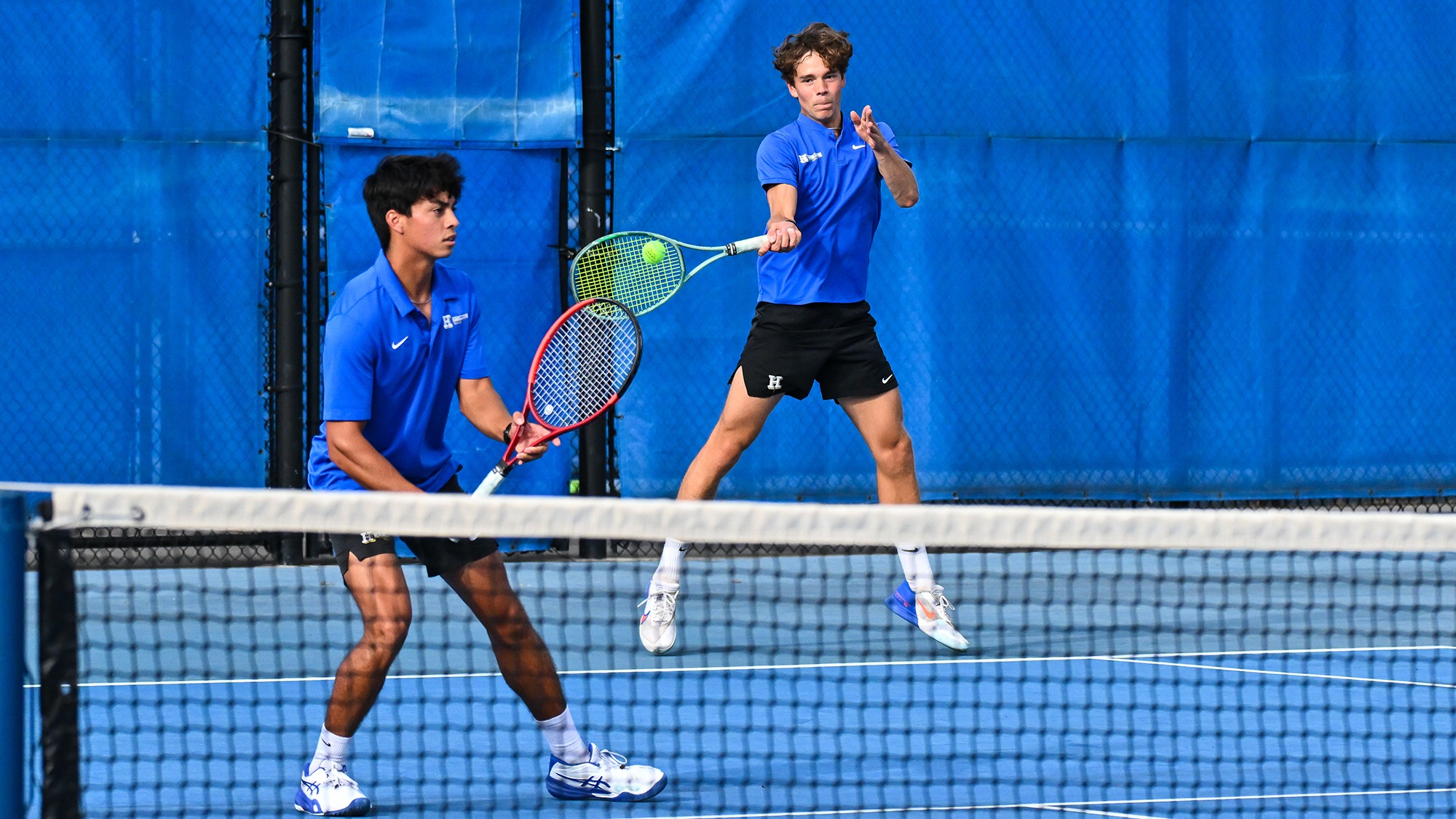 Men's Tennis player Villem Aadamsoo hits a forehand return while doubles partner Lleyton Mendieta stands near the net 