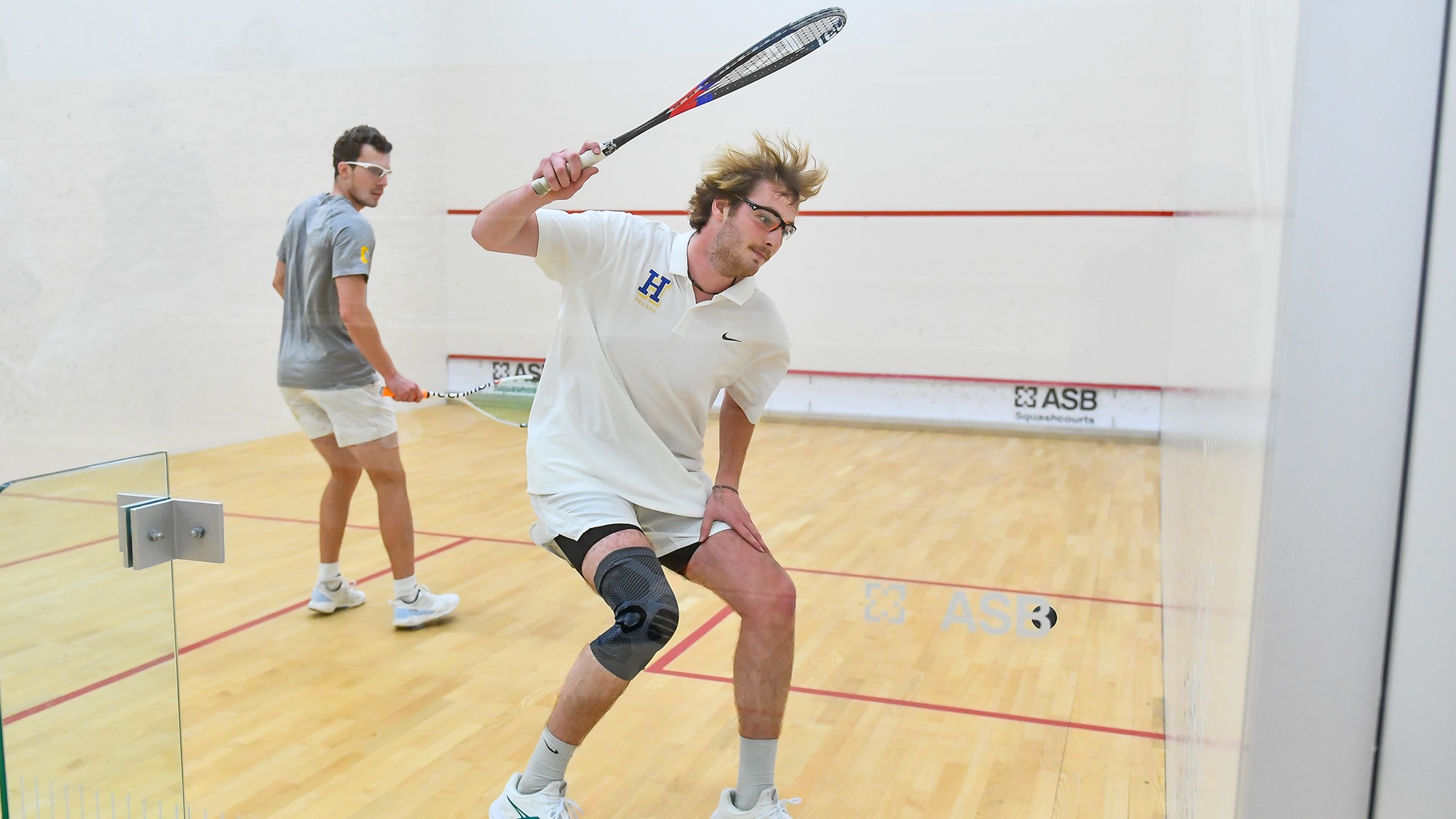 Tobey Suratt prepares to hit a return in a squash match against Williams
