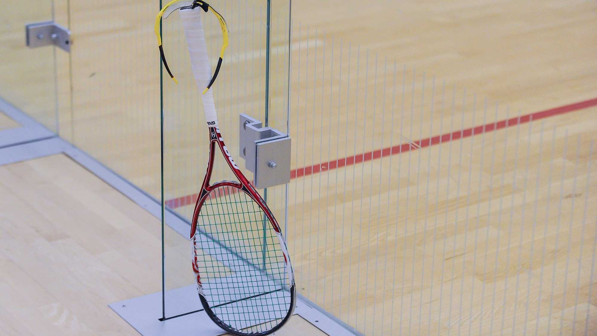 Squash glasses hang on the end of a racquet handle outside a squash court