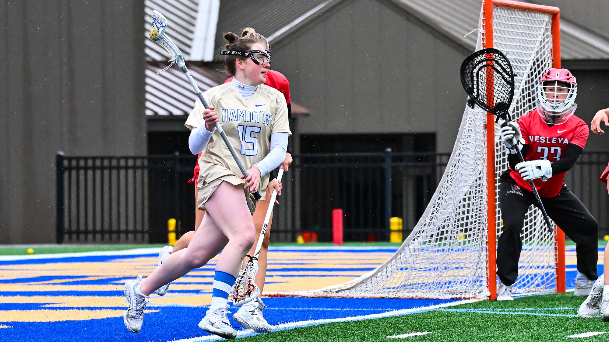 Aine Cleary looks for a women's lacrosse teammate to pass to from the goal line to the left of the crease against Wesleyan