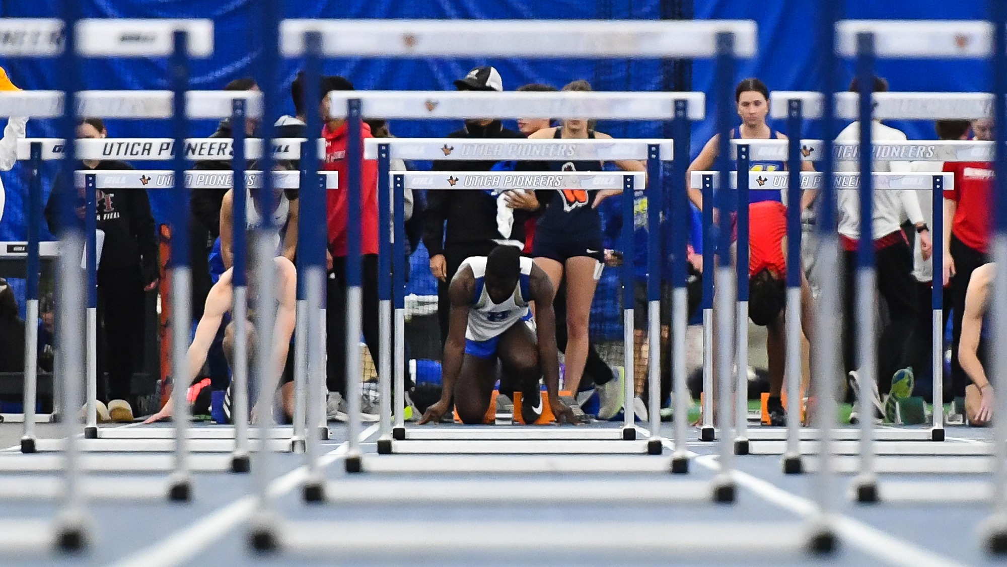 A Men's Track and Field athlete goes down on one knee before the start of the 60-meter hurdles at Utica in 2025 indoor meet