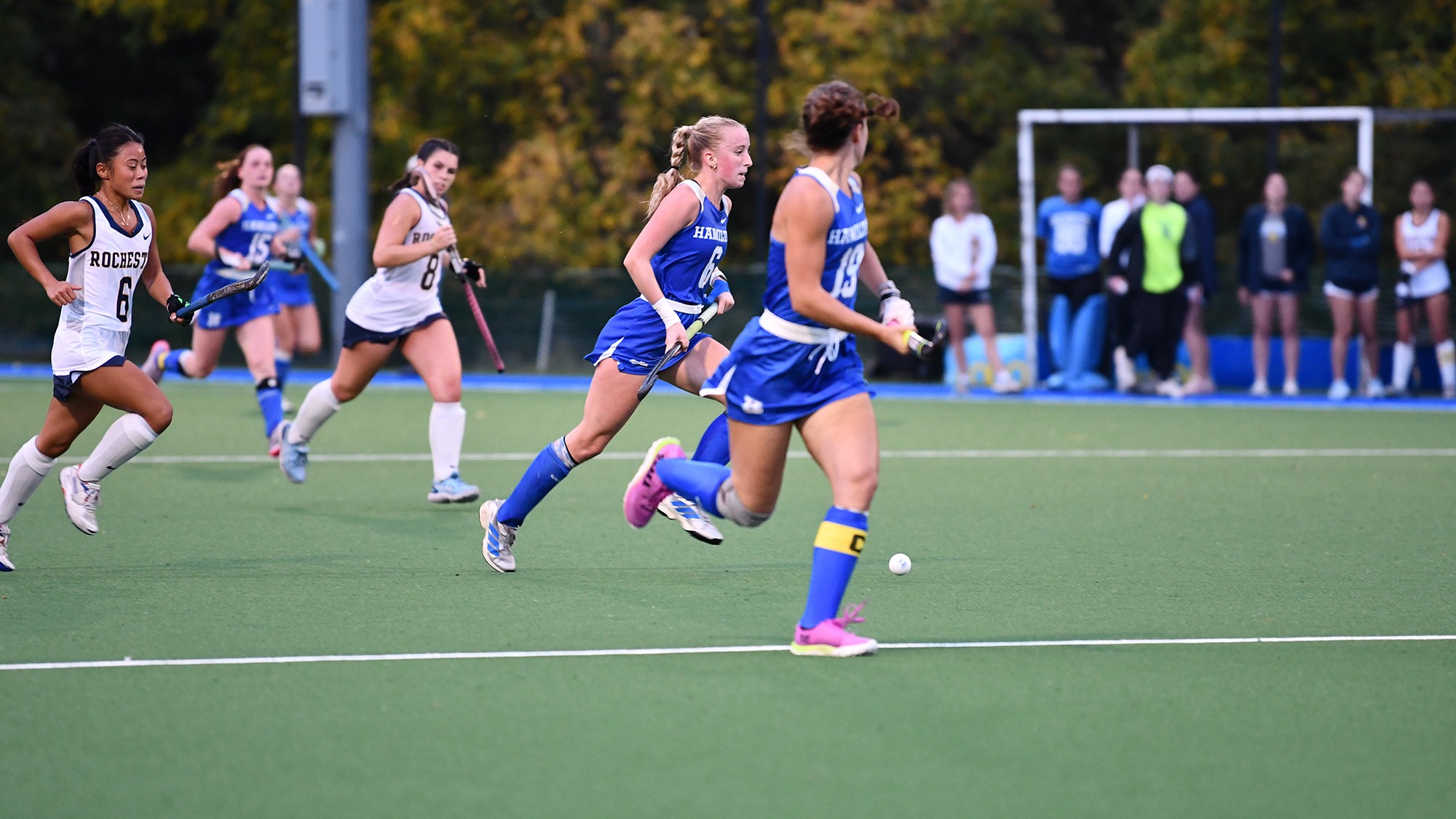 Field Hockey players rush up the field with the ball against Rochester