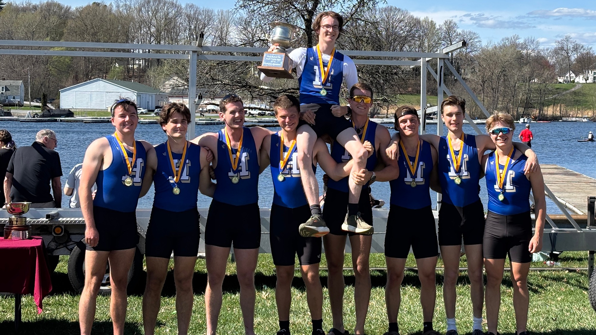 Men's Rowing team poses with gold medals and trophy for winning the varsity eight at the 2026 state championships