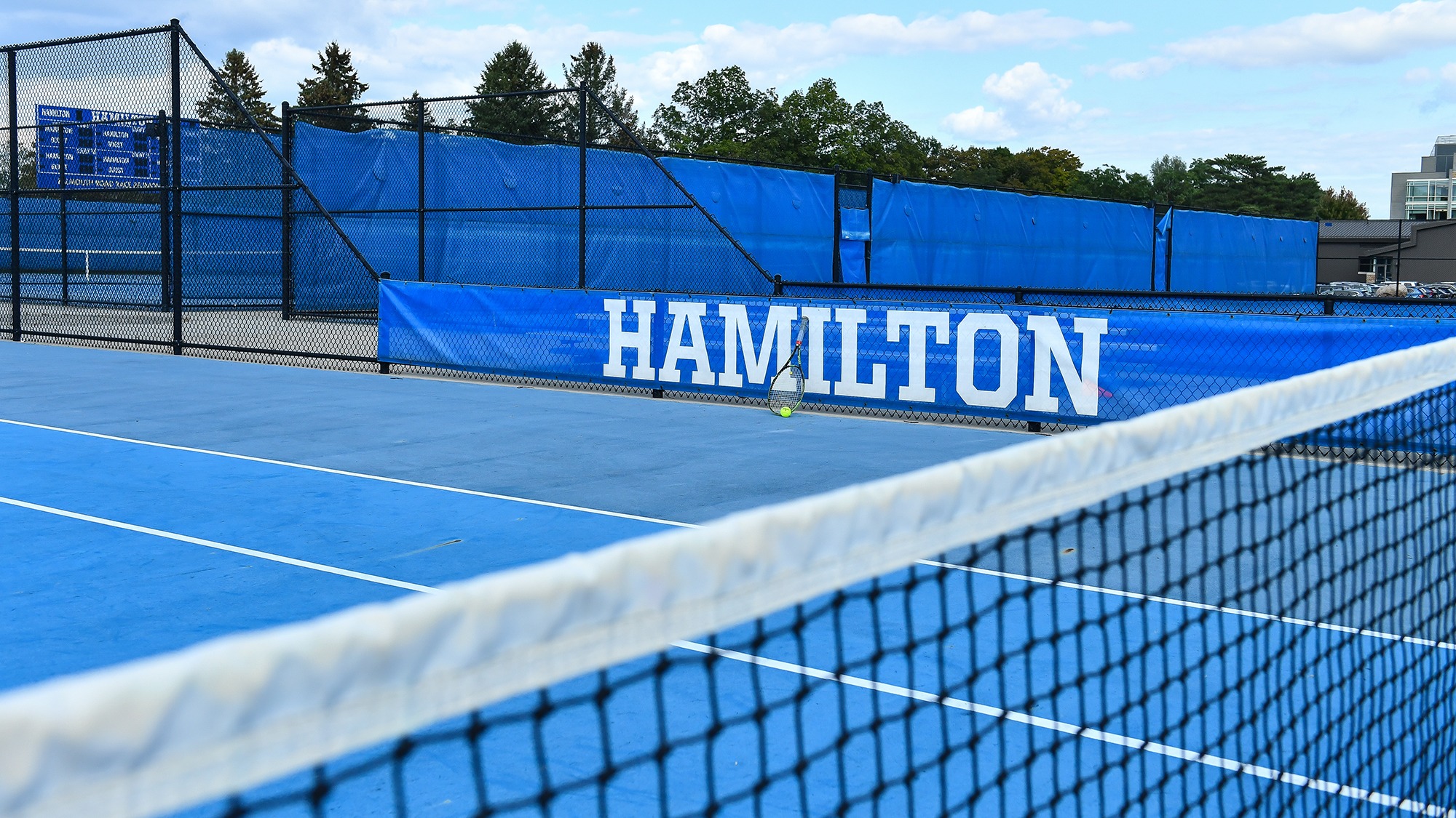 Tennis racket leans up against a Hamilton banner at Tietje Family Tennis Center