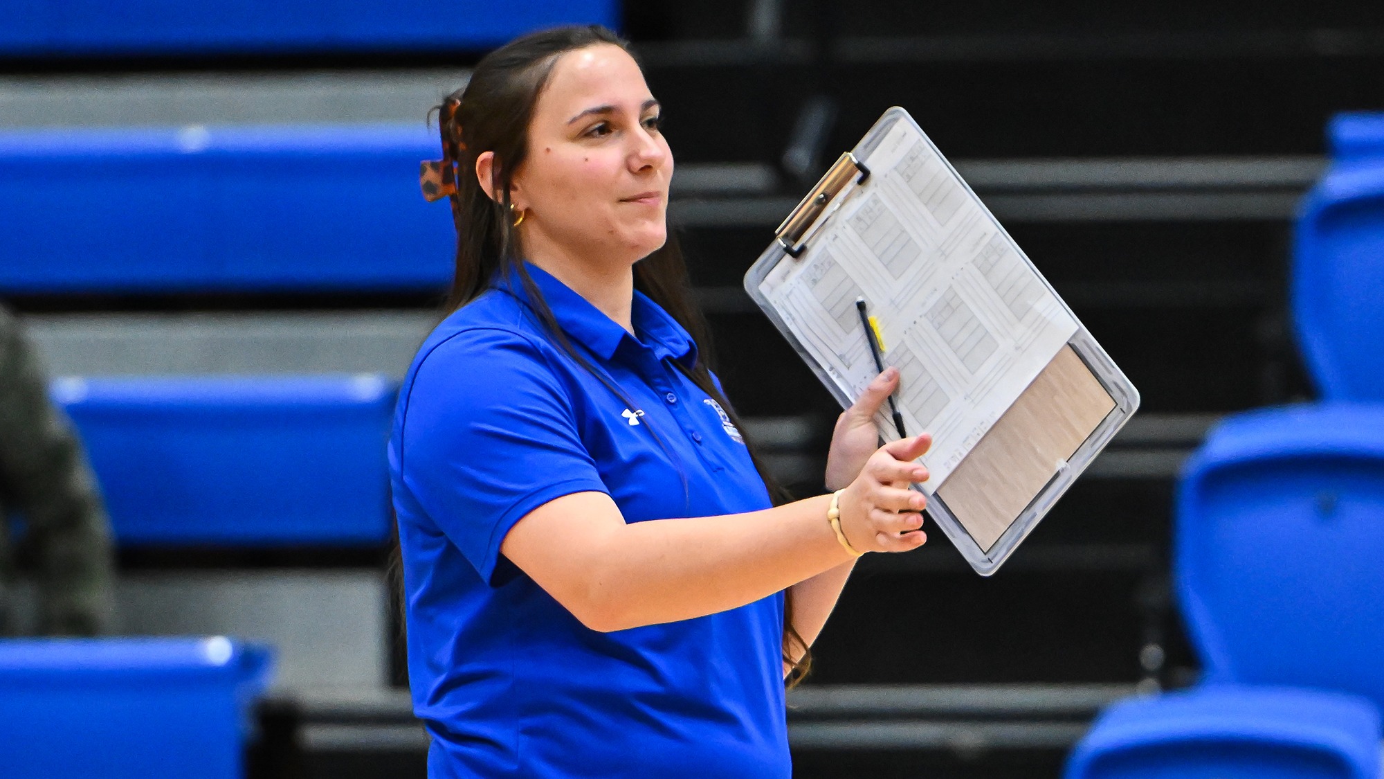 Brittany Orminski signals to a volleyball athlete while holding a clipboard on the sideline during a 2025 match