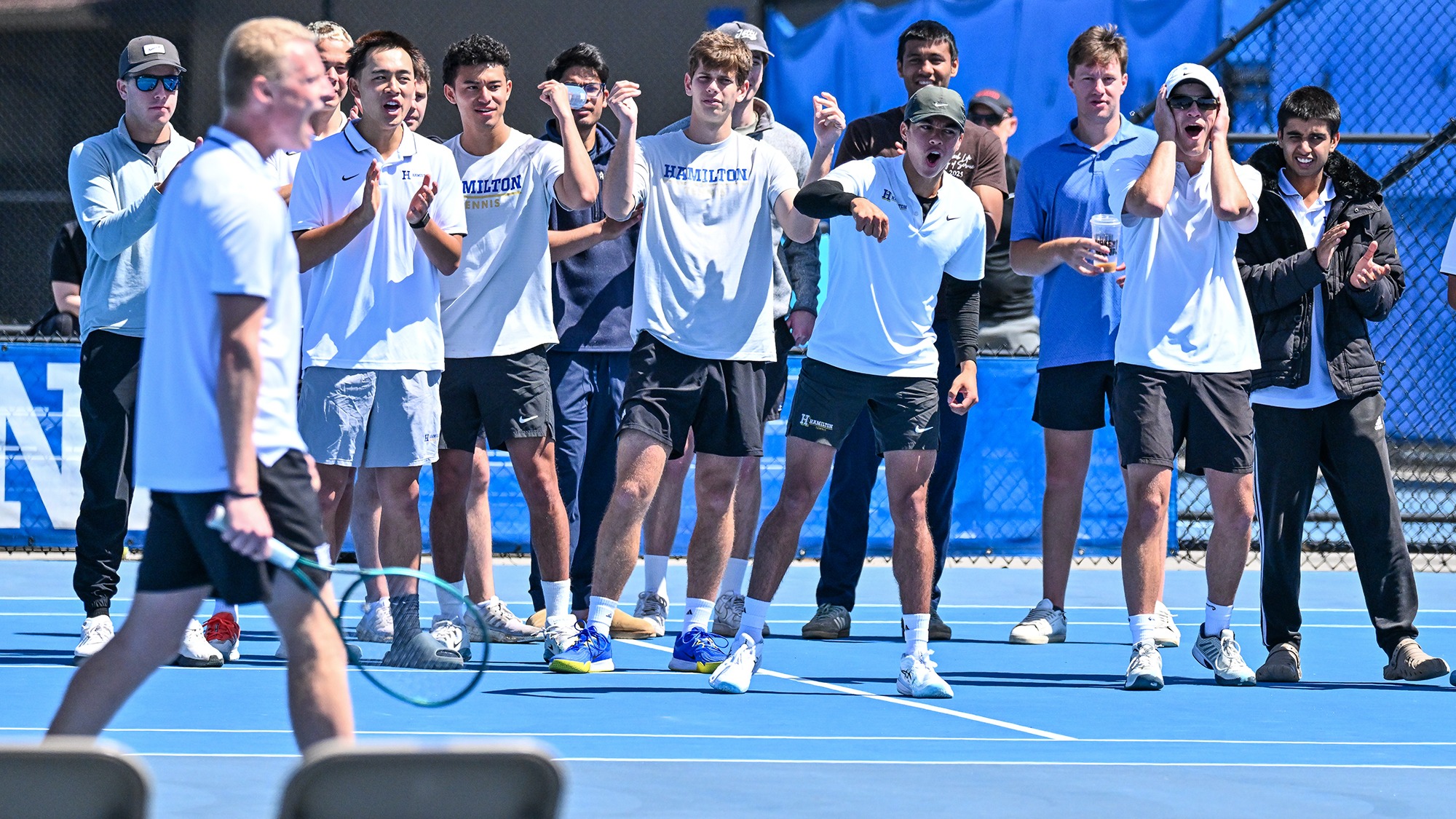 The Men's Tennis team cheers for teammates during a doubles match with Wesleyan