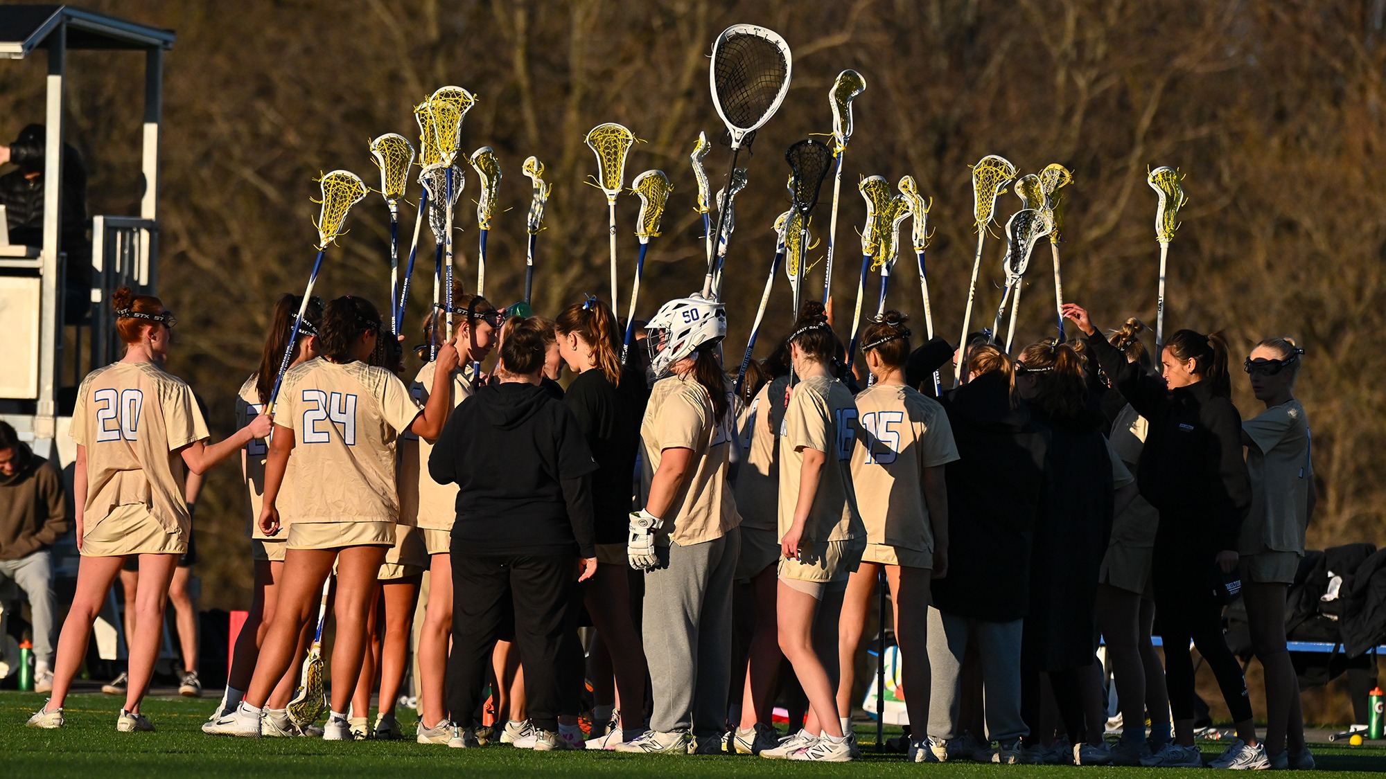 Women's Lacrosse players hold up their sticks as they break the huddle during a game with Williams