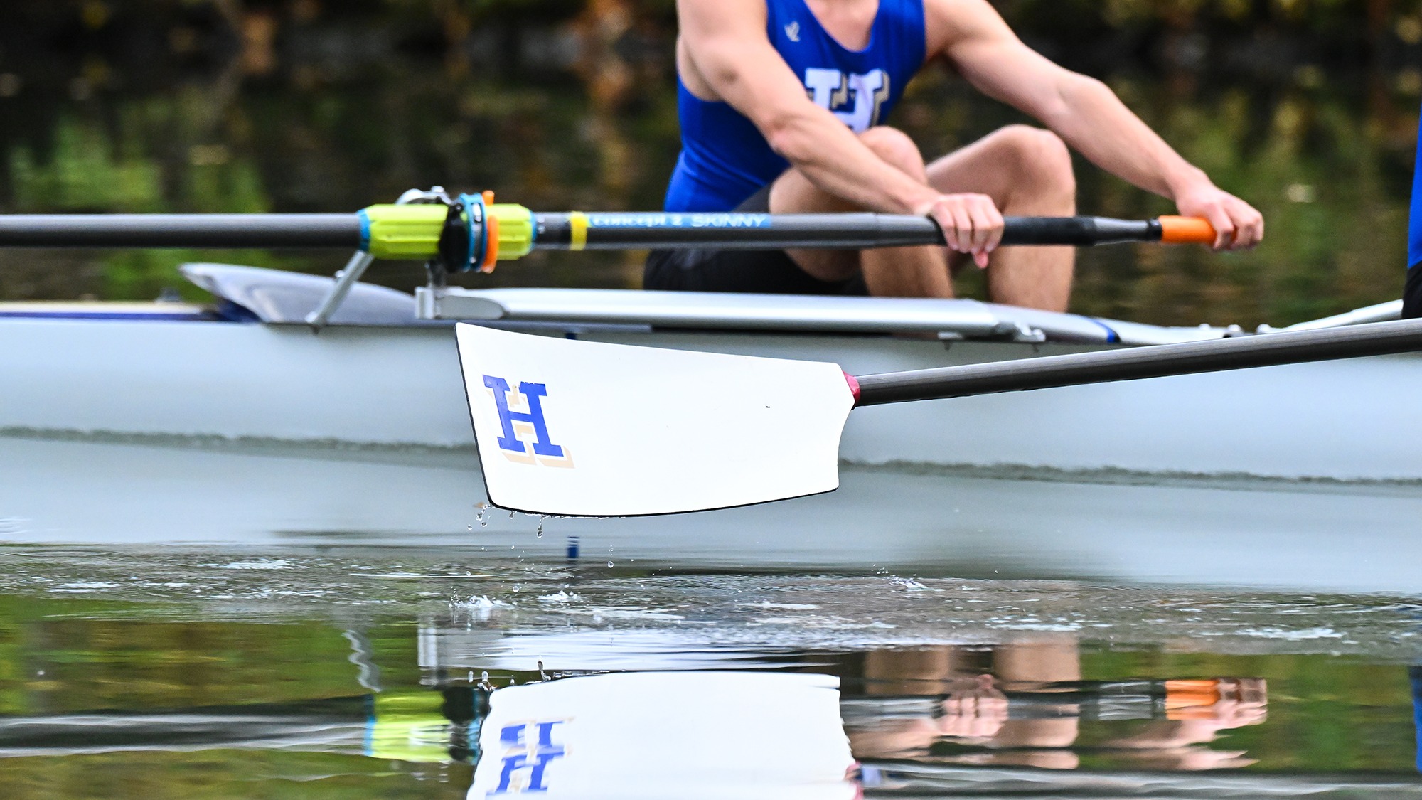 An oar hangs above the water from one of the boats during Men's Rowing practice 