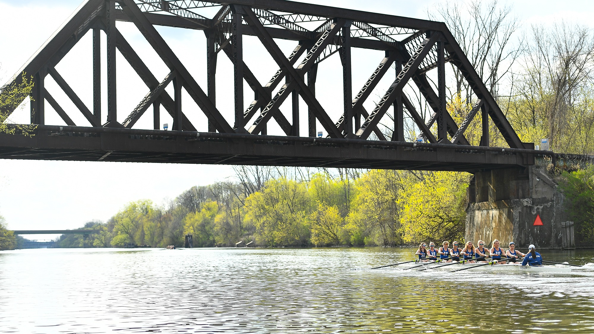 A boat passes under a bridge on the Erie Canal during Women's Rowing practice