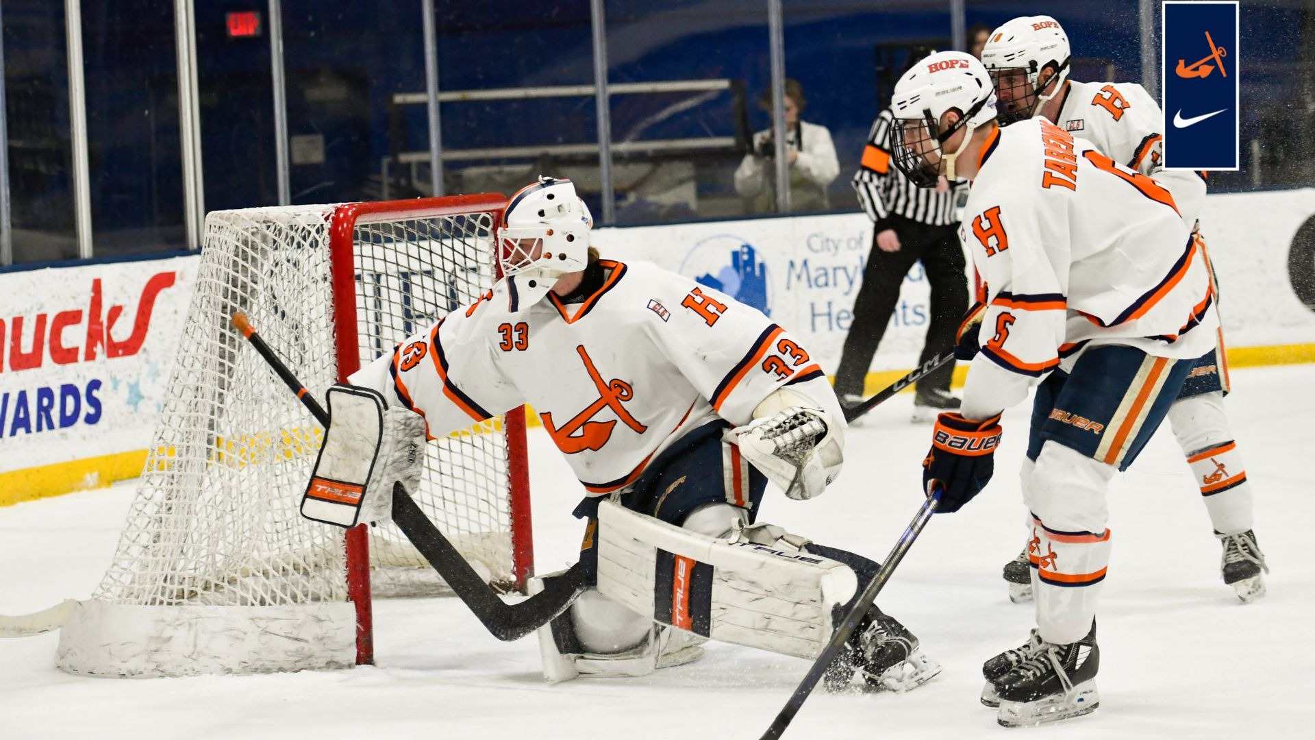 Hope's goaltender and two skaters look for the puck behind the net.