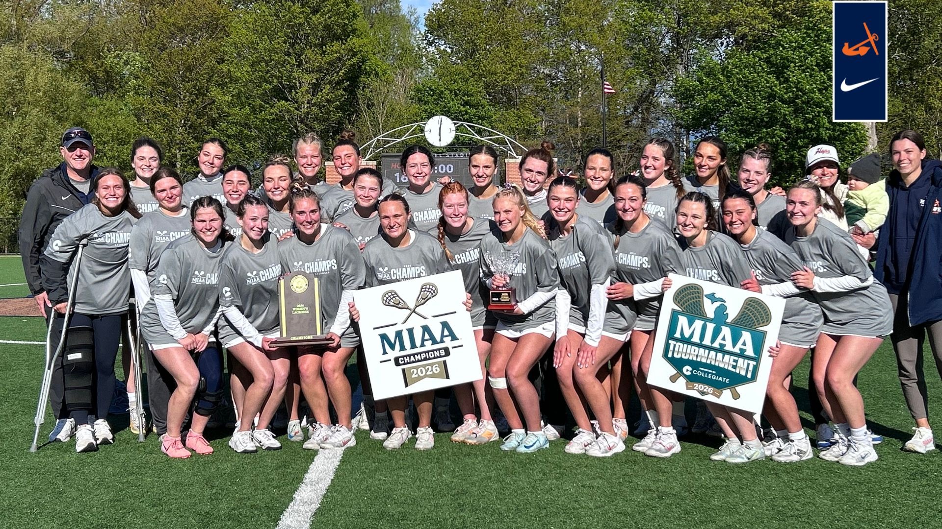 The Hope College women's lacrosse team holds the MIAA Tournament and regular-season trophies at Van Andel Stadium.