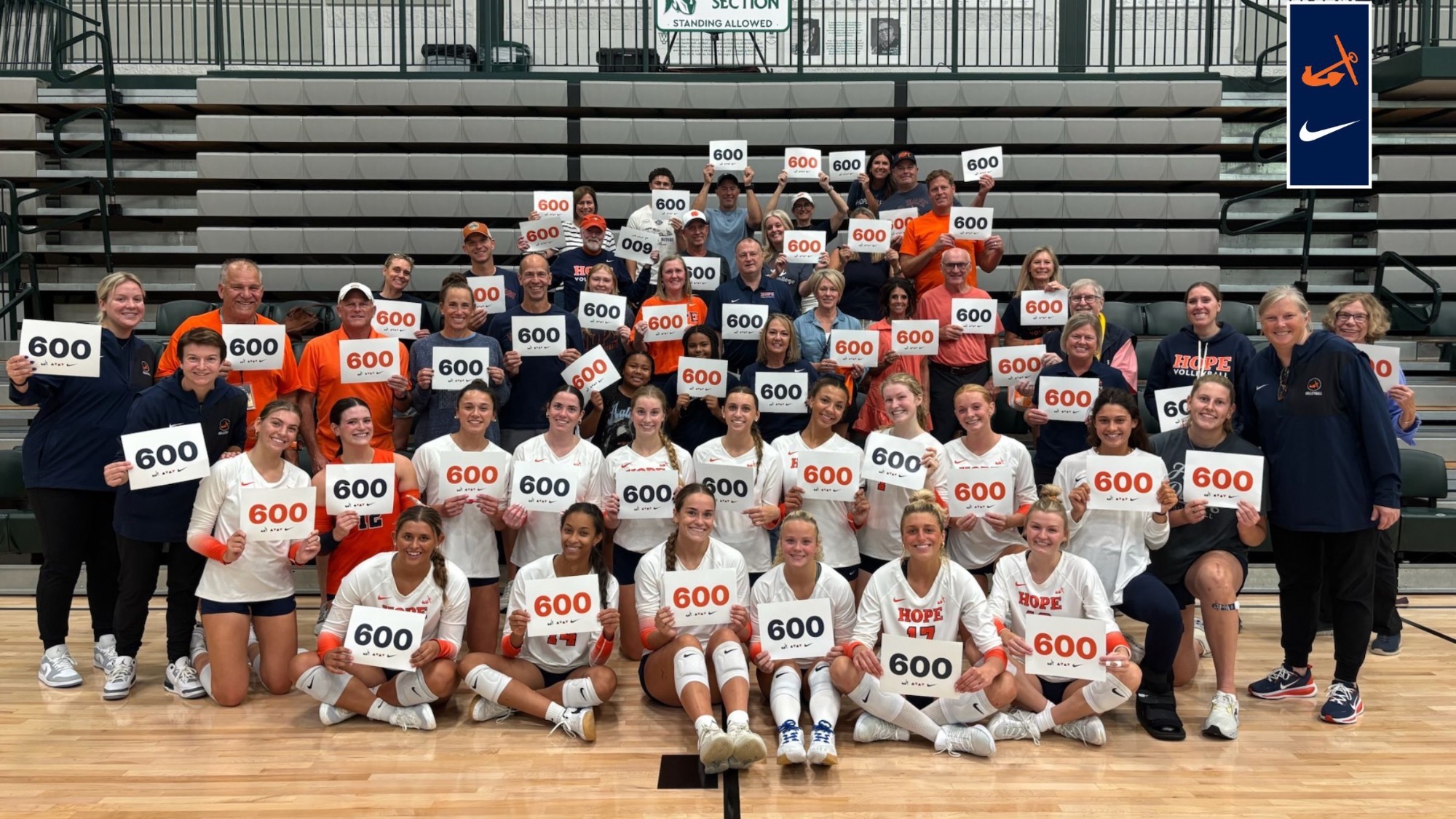 Hope College volleyball team holds 600 signs in celebration of head coach Becky Schmidt's 600th coaching victory.