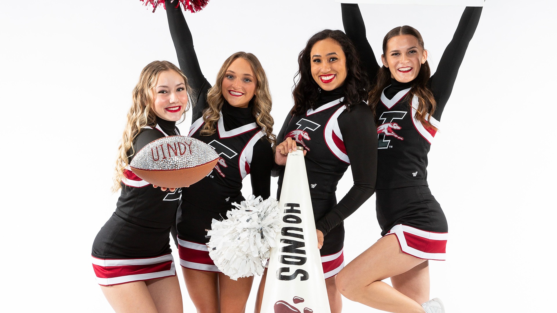 Members of the UIndy cheerleading team pose with a football, signage, and pom poms.