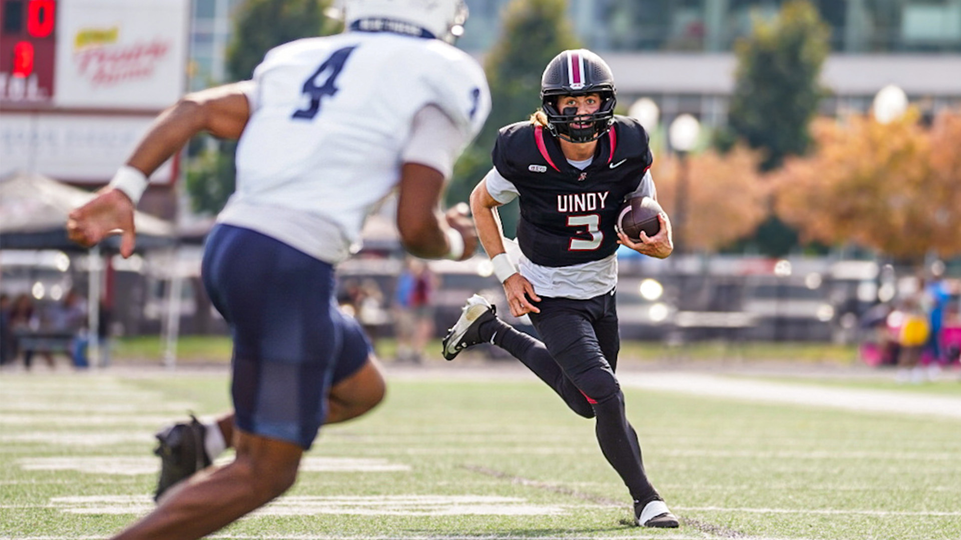 UIndy quarterback Gavin Sukup running the ball with a defender in front of him.