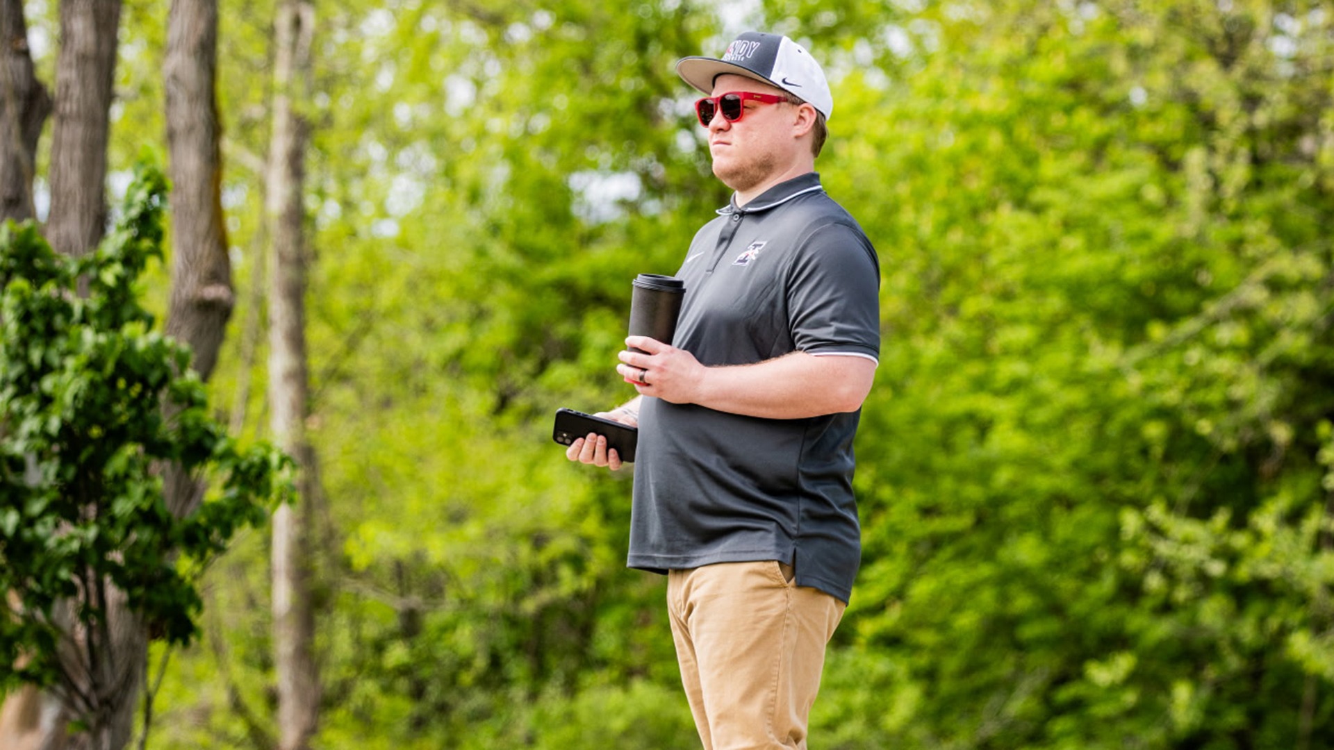 Cody Wainscott with coffee and phone in hand watching UIndy women's lacrosse