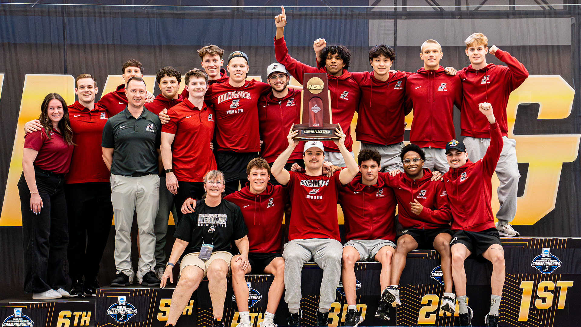 The UIndy men's swimming and diving teams posing them their fourth-place trophy at the 2026 NCAA DII Championships.