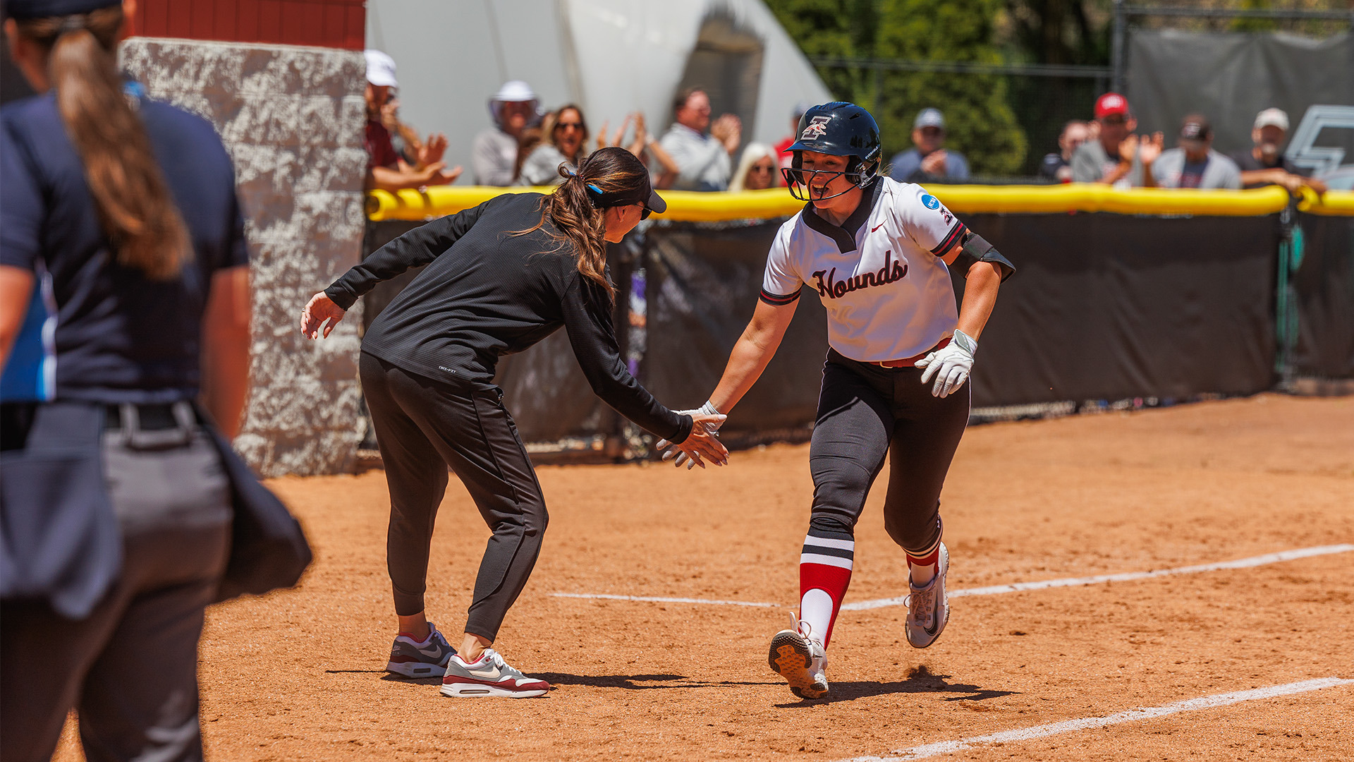 Paige Vickery low-fives Coach Frost rounding third on her home run versus Tiffin at the NCAA Regional.