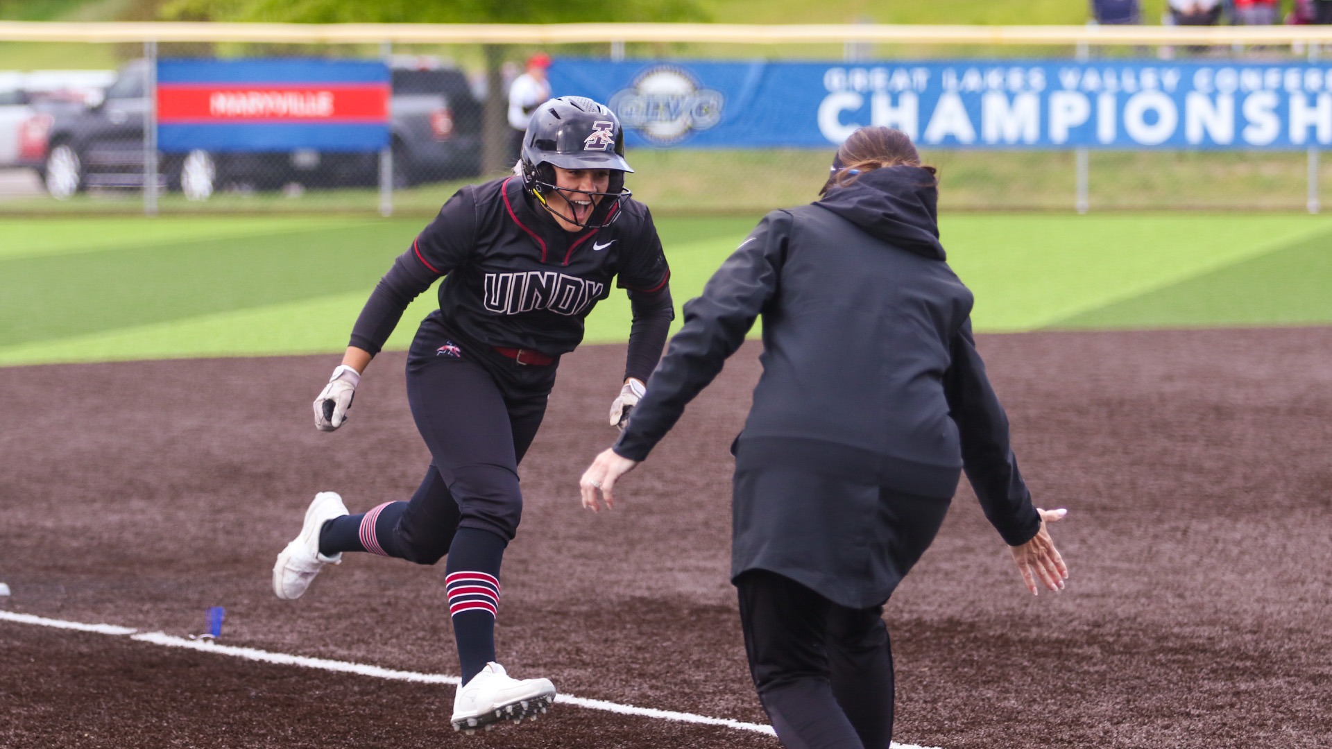 UIndy softbaall student-athlete Brooklyn Wills rounds third base on her home run trot, set to give a low-five to head coach Melissa Frost.