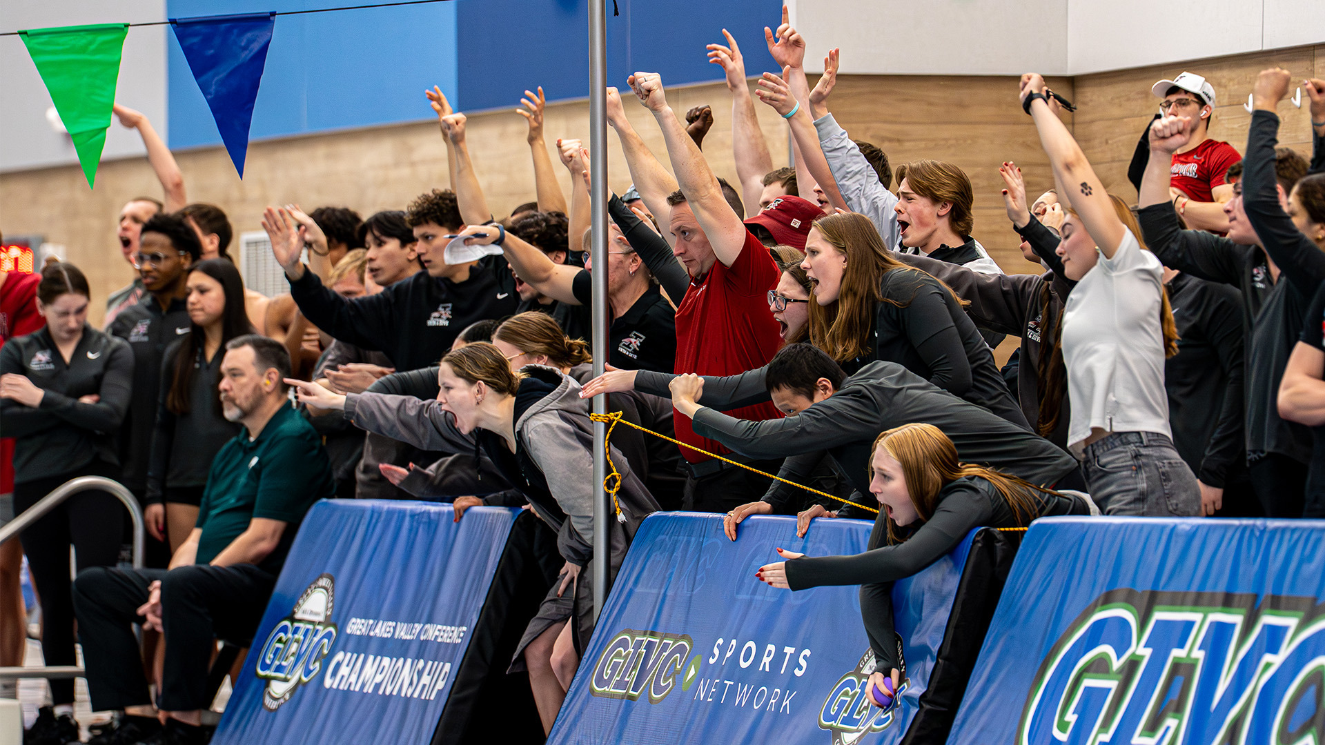 Members of the UIndy swimming and diving team standing poolside at the 2026 GLVC Championships, cheering on their teammates.