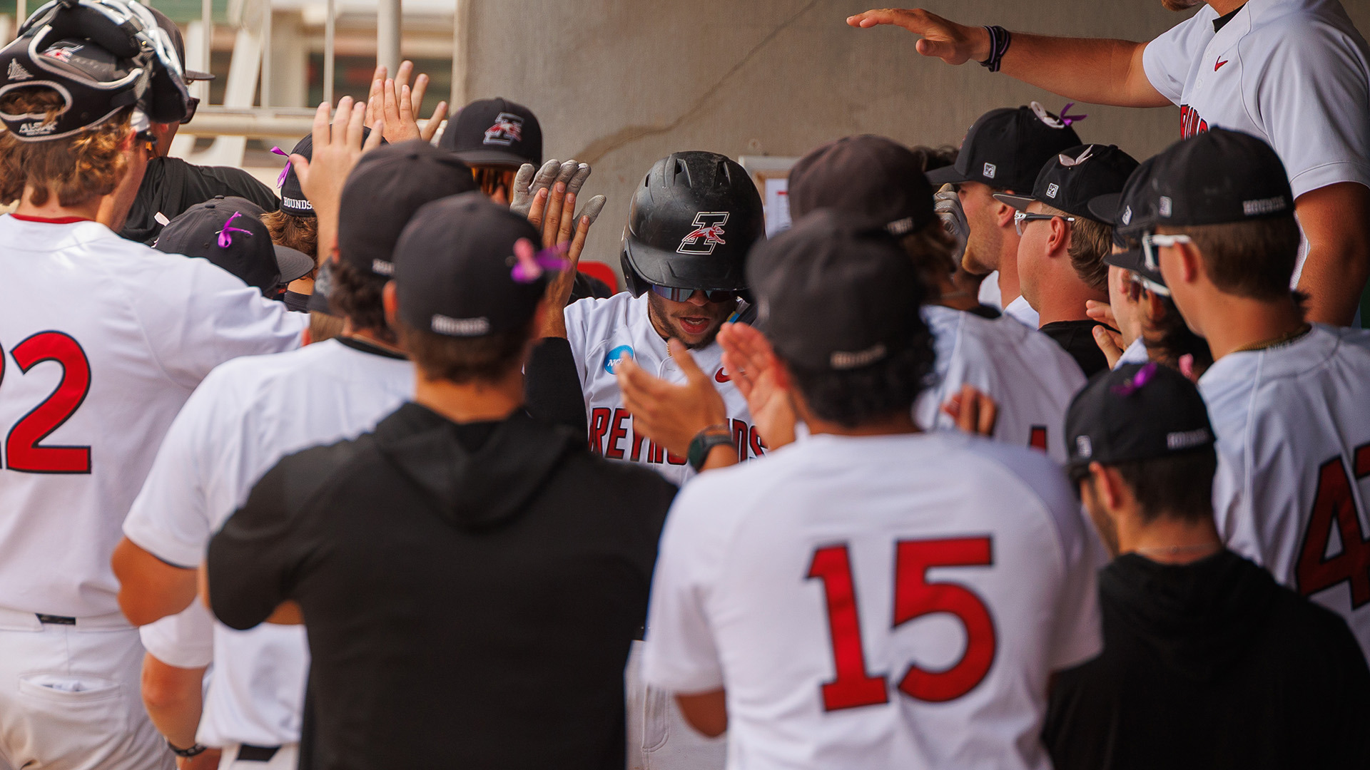 UIndy baseball student-athlete Chase Mason walking through the dugout being congratulated by teammates after scoring a run.