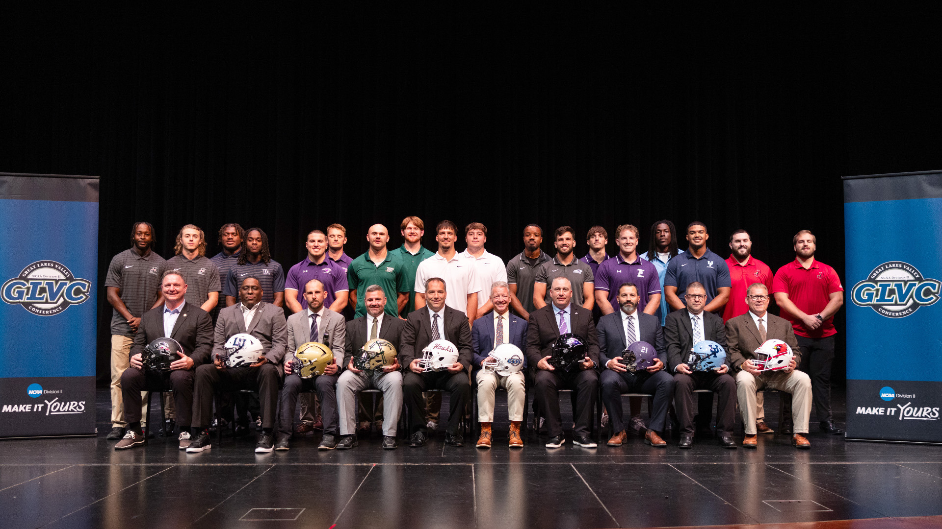 18 student-athletes and nine head coaches from nine member instistutions as well as Commissionor Jum Naumovich pose on-stage during the 2025 GLVC Football Kickoff event.
