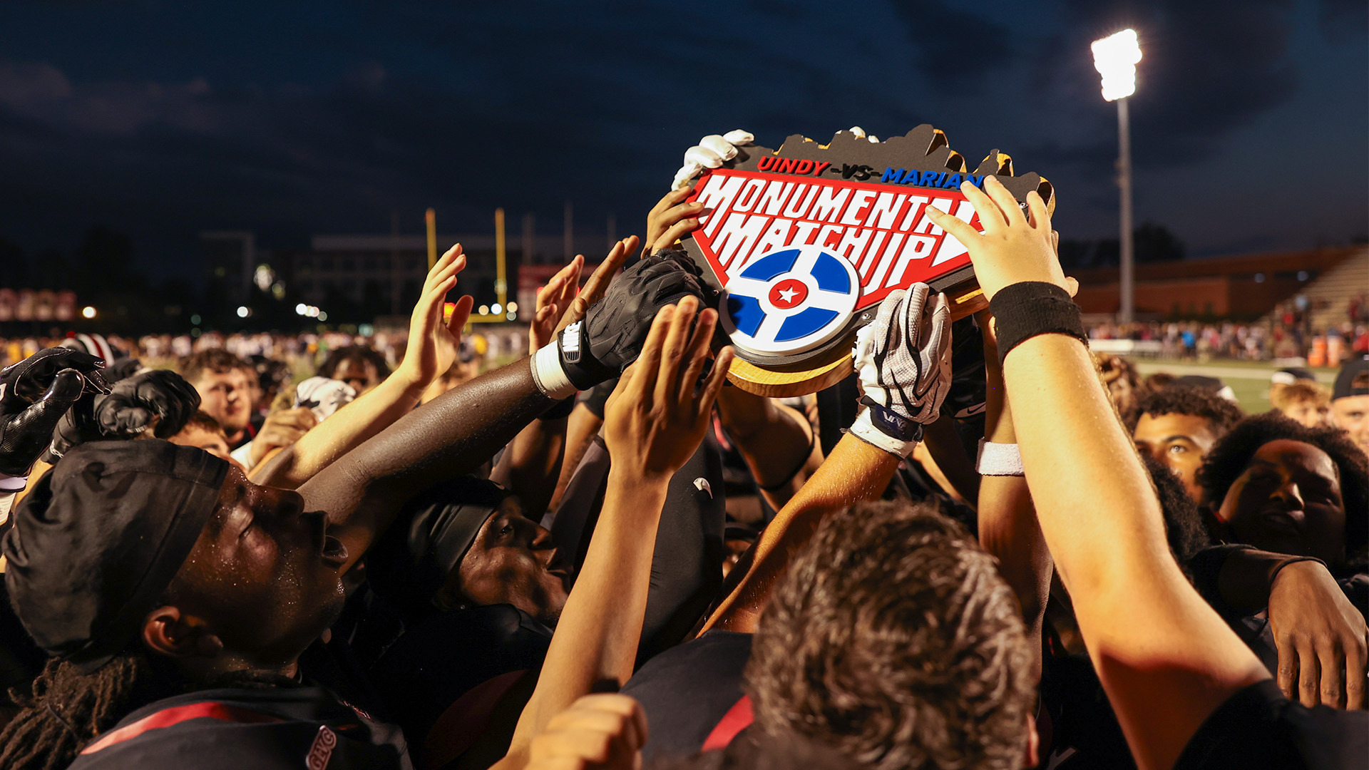 Members of the UIndy football team hold up the Monumental Matchup trophy in victory.