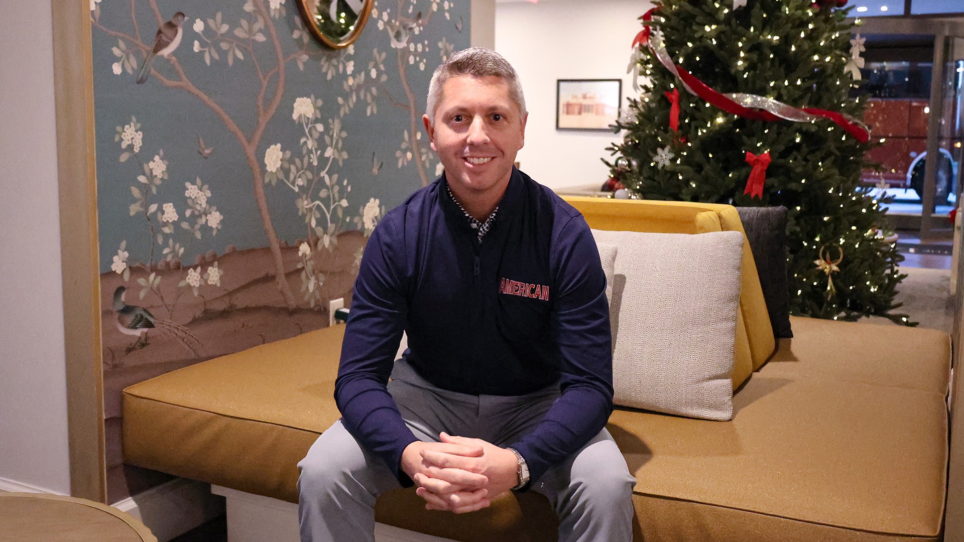 Director of Athletics JM Caparro sitting in a holiday-decorated hotel lobby