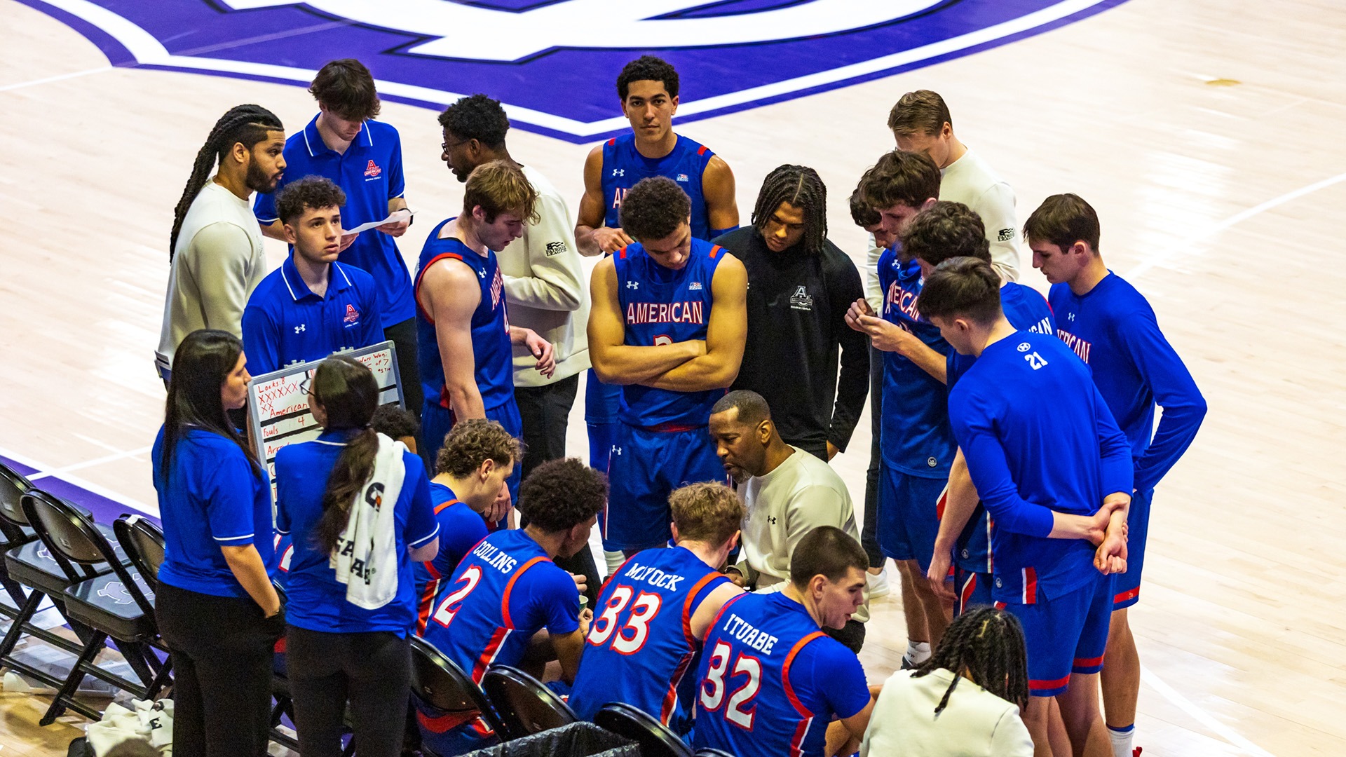 men's basketball team huddled during a timeout listening to coach Duane Simpkins