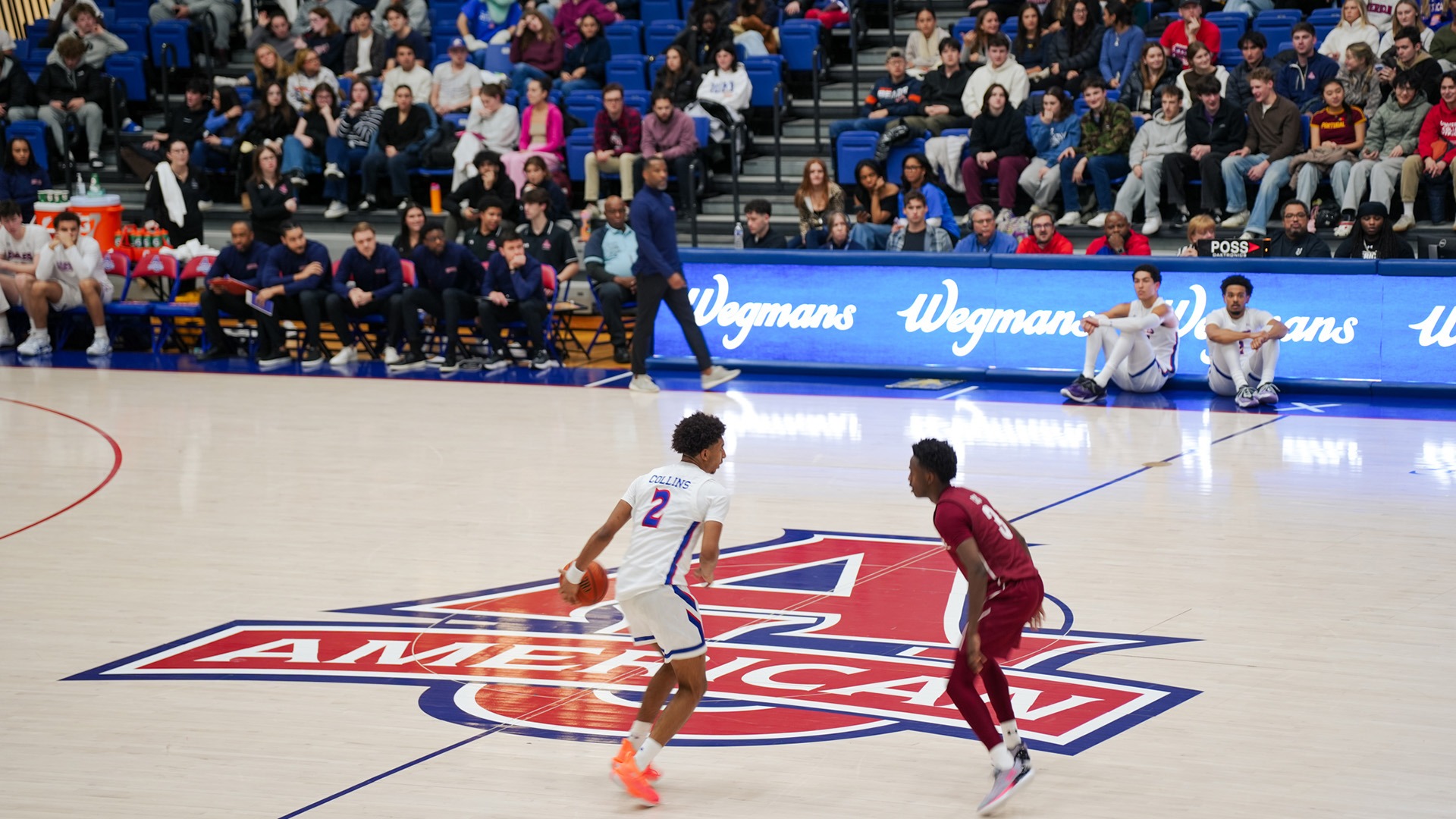 Madden Collins dribbling the ball at a men's basketball game with the student crowd in the background
