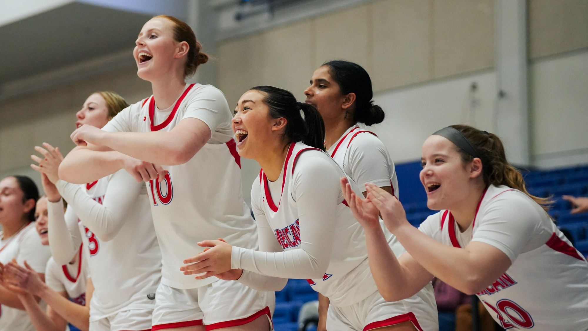 Women's basketball bench celebrating a three-point shot.