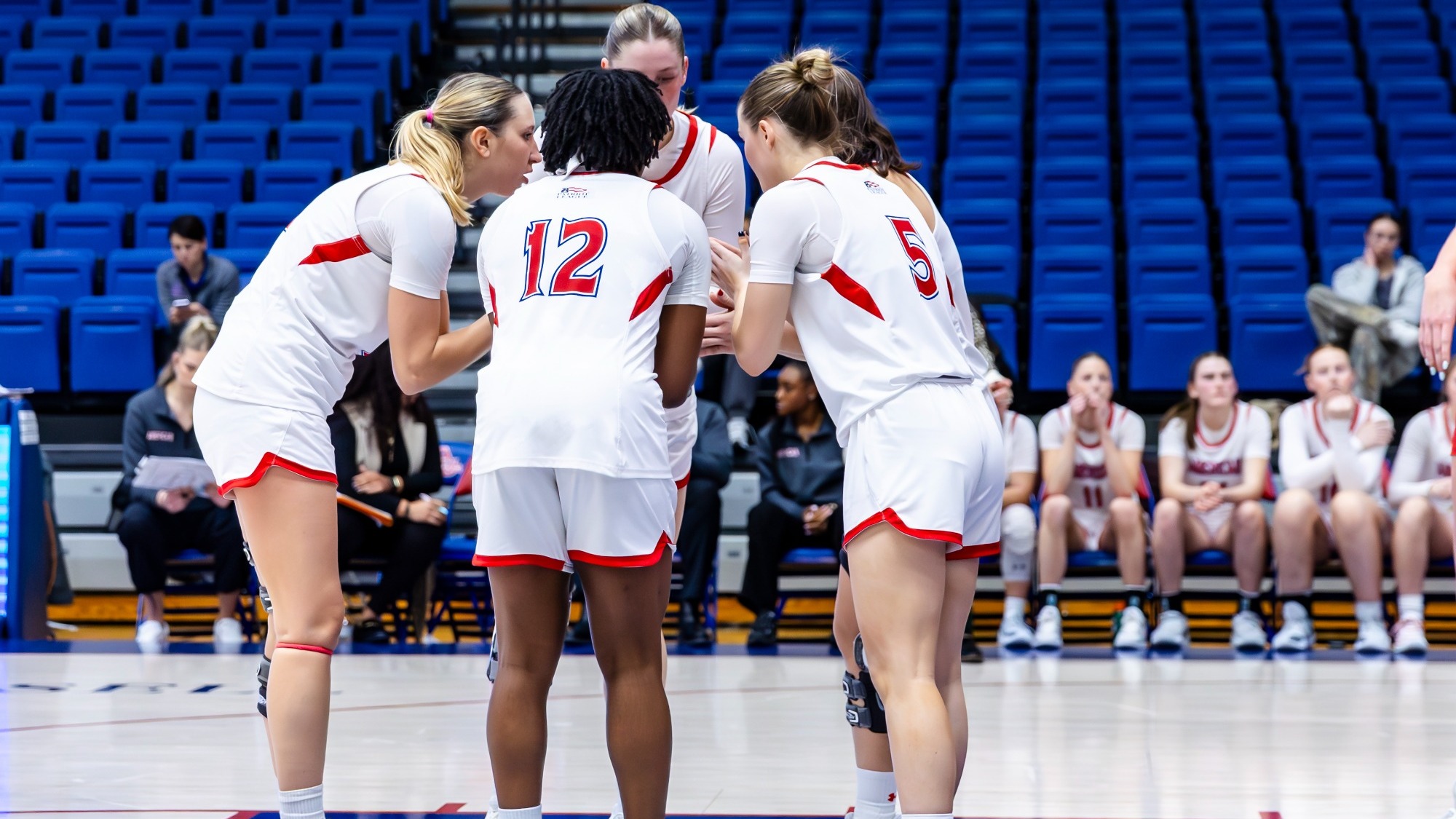 Women's basketball on court players huddle together during a break in play.